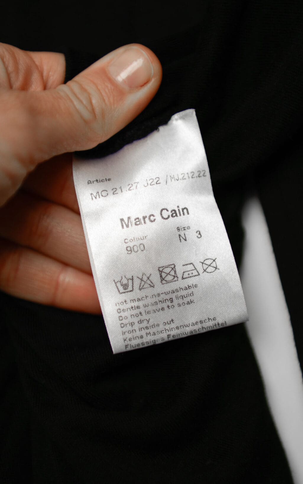 Schwarzes Marc Cain Kleid aus Modal und Seide mit Raffung im Brustbereich, langärmelig, figurbetont geschnitten, auf weißem Hintergrund hängend.