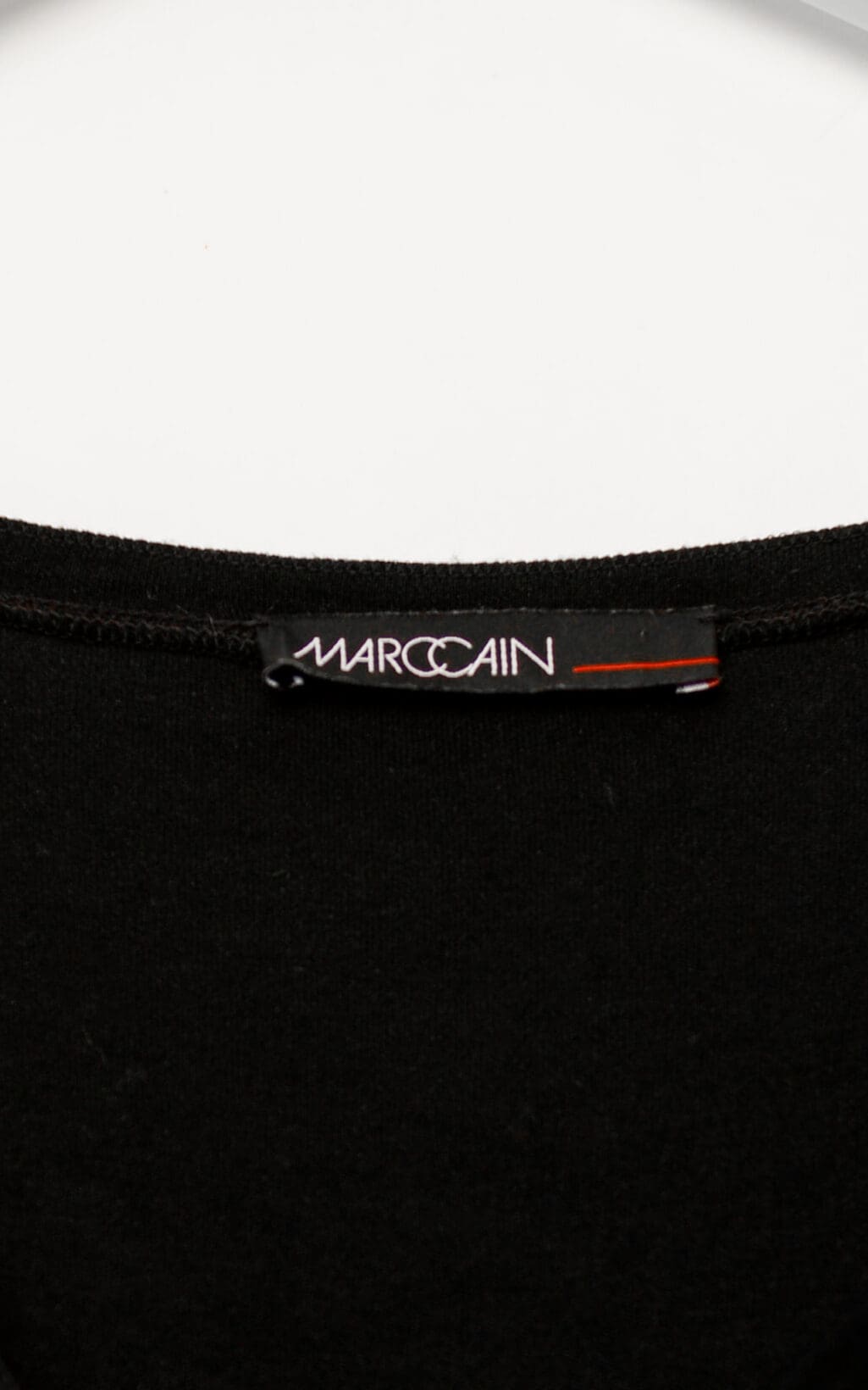 Schwarzes Marc Cain Kleid aus Modal und Seide mit Raffung im Brustbereich, langärmelig, figurbetont geschnitten, auf weißem Hintergrund hängend.