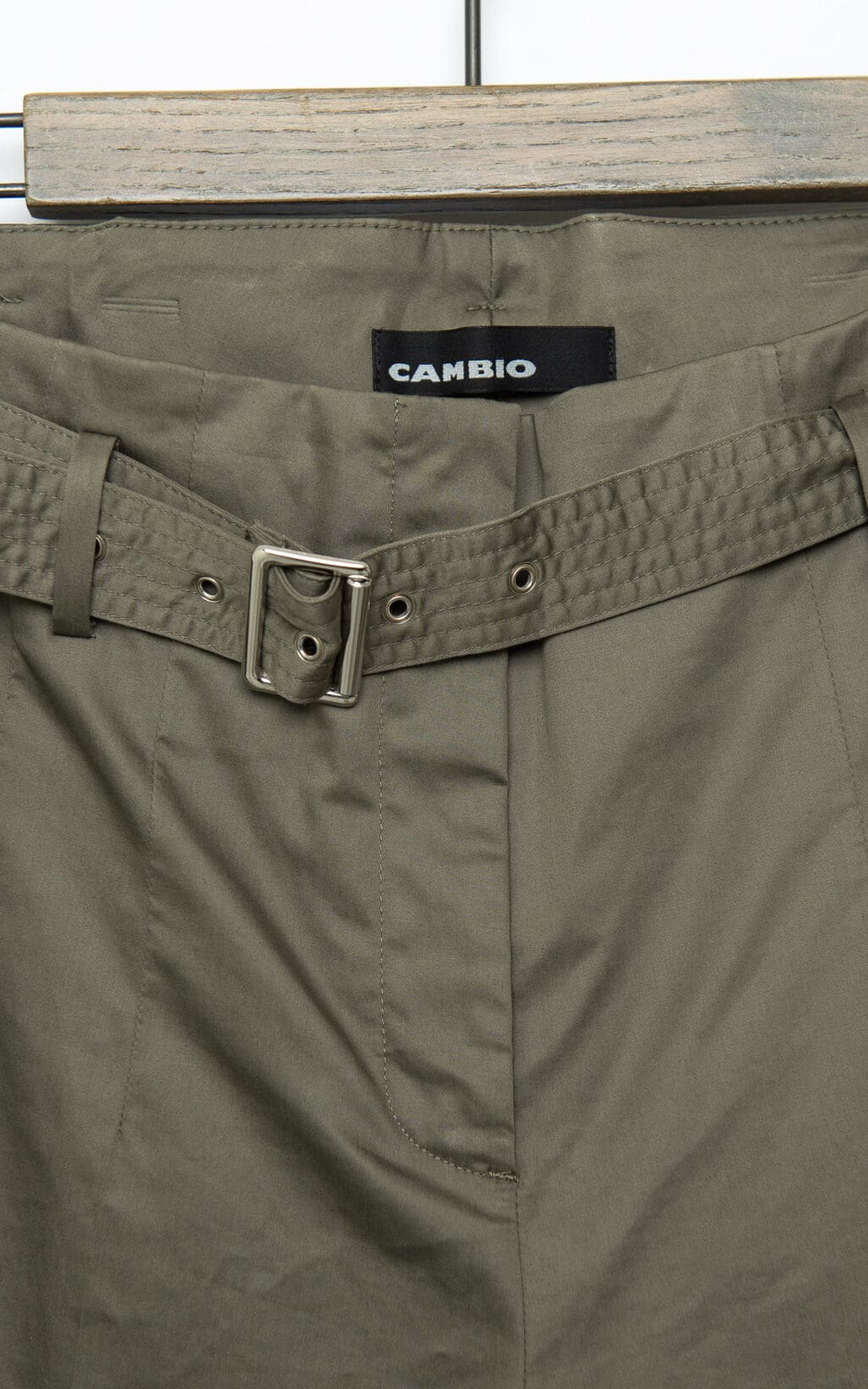 Die olivgr&uuml;ne Hose hat einen passenden G&uuml;rtel mit silberner Schnalle, h&auml;ngt auf einem Holzb&uuml;gel und tr&auml;gt das Etikett &bdquo;CAMBIO Hose &ndash; Gr. 38&ldquo;. Der Stoff wirkt leicht.