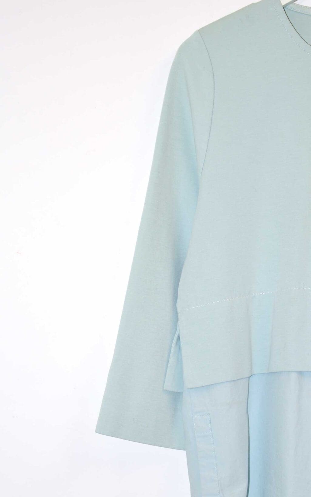 Hellblaues COS Damen-Top mit 3/4-&Auml;rmeln, asymmetrischem Lagen-Look und einer wei&szlig;en aufgesetzten Brusttasche. Hochwertiges Secondhand-Designer-Teil, verf&uuml;gbar auf Monkky.ch.