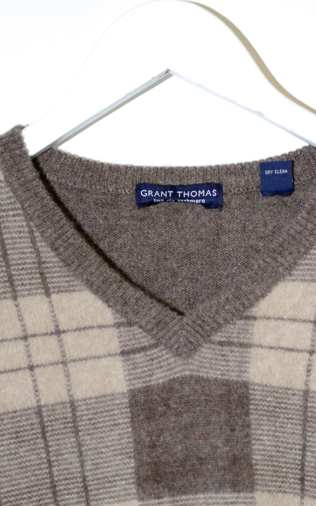 Secondhand Kaschmirpullover mit V-Ausschnitt in Braun- und Beiget&ouml;nen, kariertes Muster, locker geschnitten. H&auml;ngt auf einem wei&szlig;en Kleiderb&uuml;gel, Etikett mit &bdquo;Grant Thomas&ldquo; sichtbar.