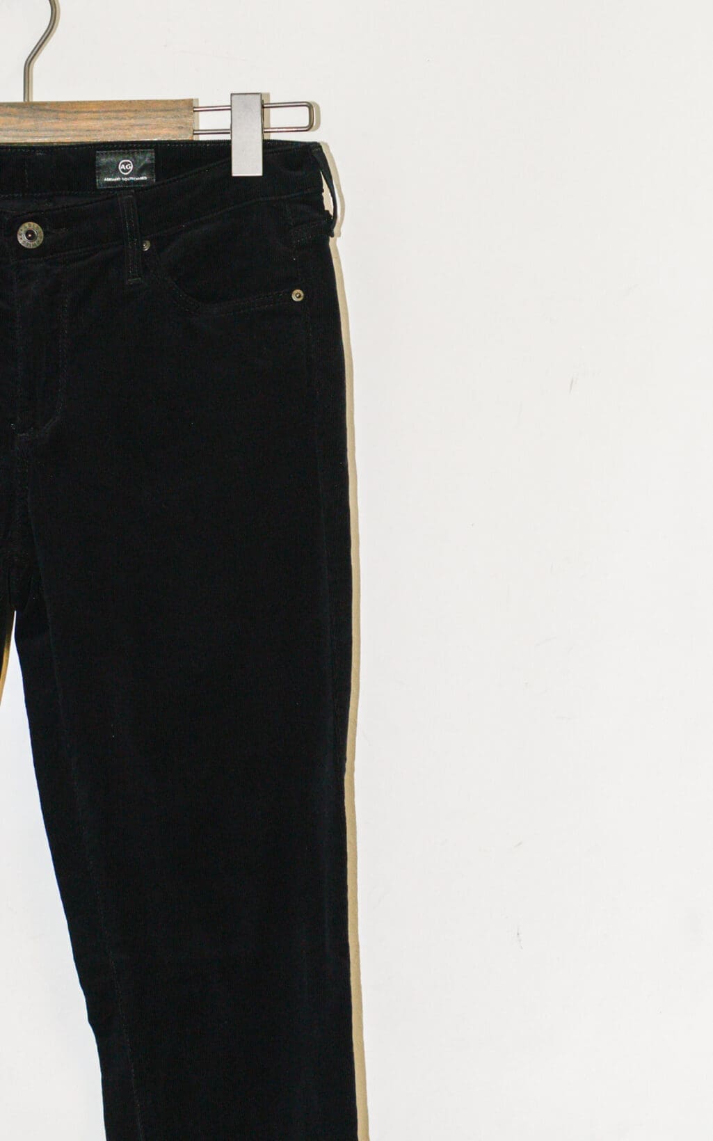 Das Adriano Goldschmied Cigarette Leg &ndash; W27 in Schwarz h&auml;ngt auf einem h&ouml;lzernen Kleiderb&uuml;gel vor einem schlichten wei&szlig;en Hintergrund, wobei nur die linke H&auml;lfte der Hose sichtbar ist.