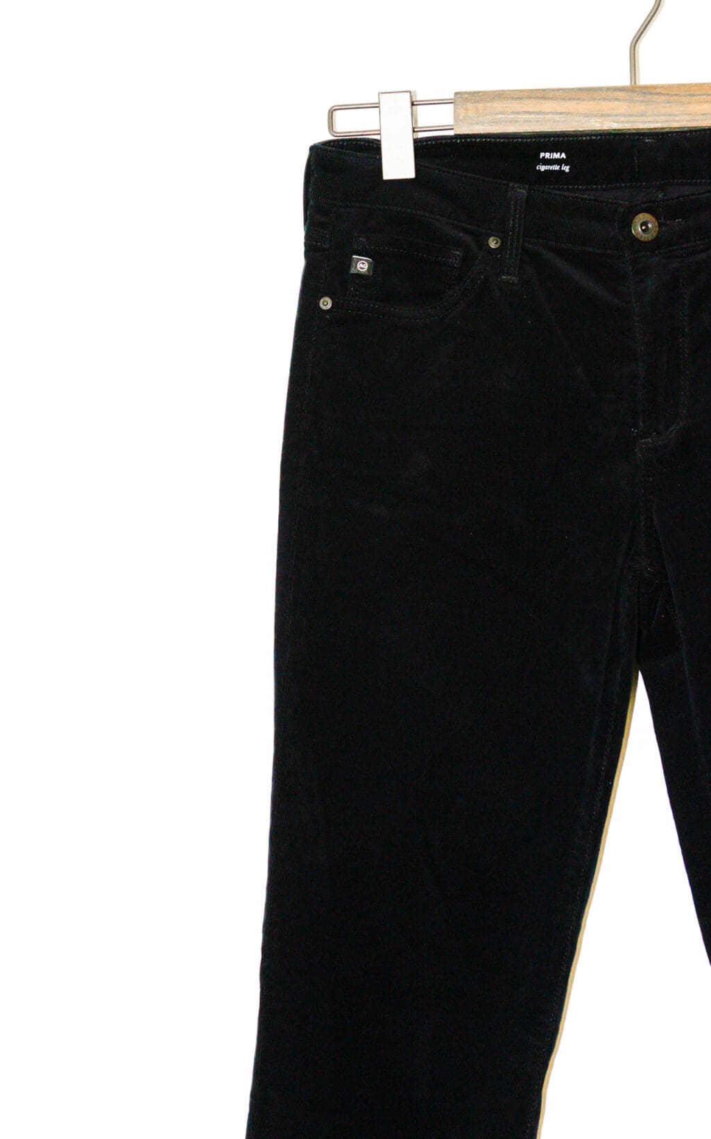 Die schwarze Cordhose &bdquo;Cigarette Leg &ndash; W27&ldquo; von Adriano Goldschmied h&auml;ngt auf einem h&ouml;lzernen Kleiderb&uuml;gel vor einem wei&szlig;en Hintergrund und zeigt die obere H&auml;lfte und die Details der Vordertasche.