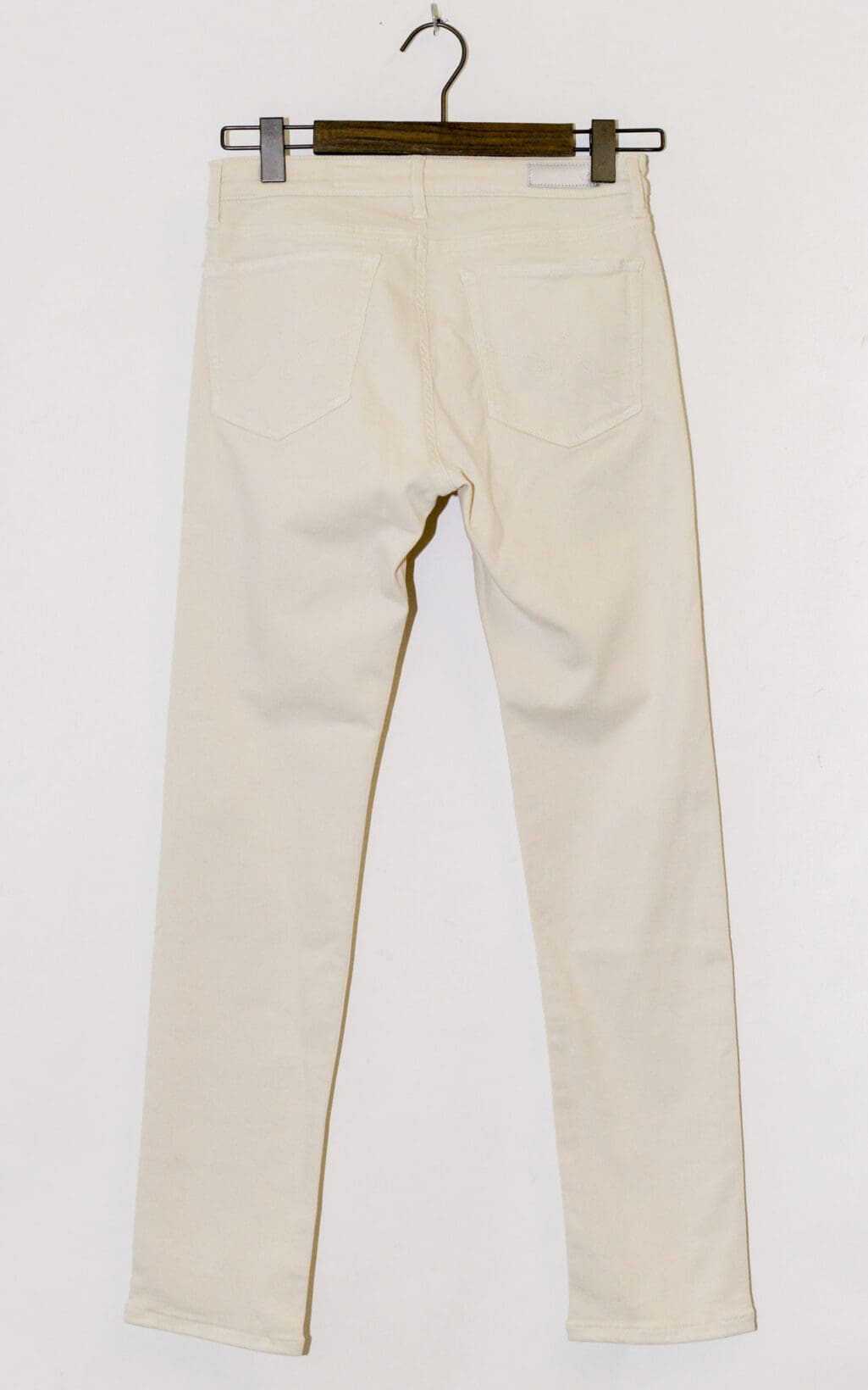 Die Adriano Goldschmied Prima Ankle Jeans (W27) in Off-White h&auml;ngen auf einem schwarzen Kleiderb&uuml;gel vor wei&szlig;em Hintergrund und zeigen die R&uuml;ckansicht mit zwei Ges&auml;&szlig;taschen.