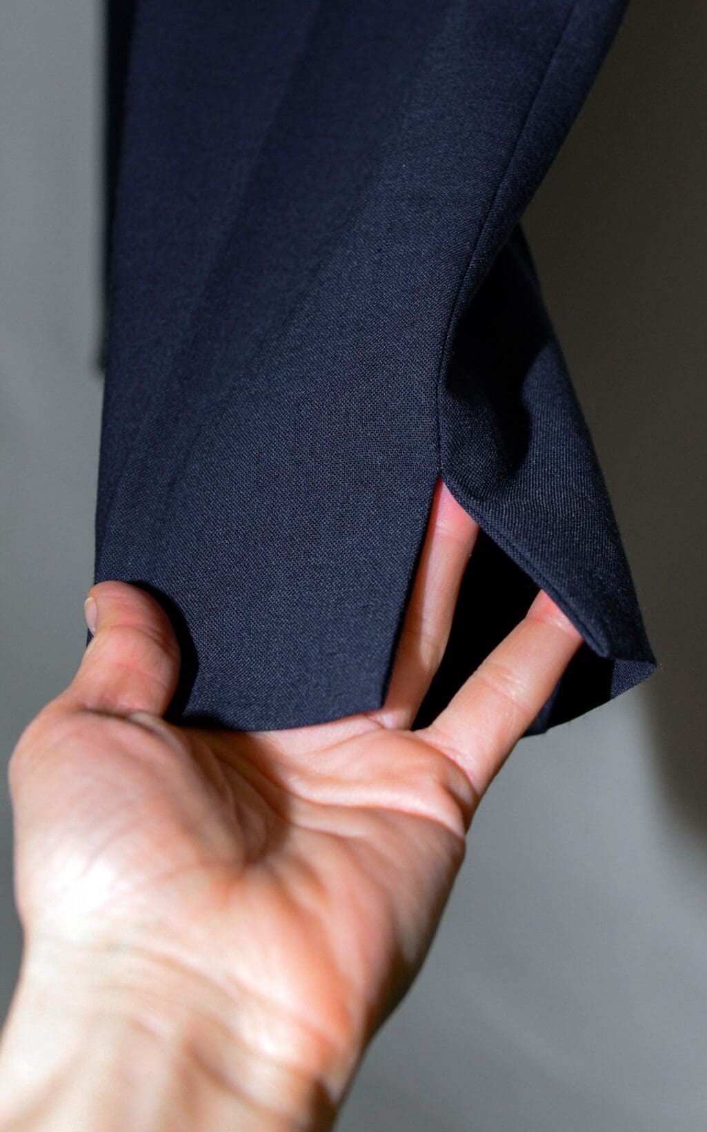 Eine Hand hebt den Saum der Closed Arlo Hose -W26 an und gibt einen kleinen Schlitz im dunklen Stoff frei.