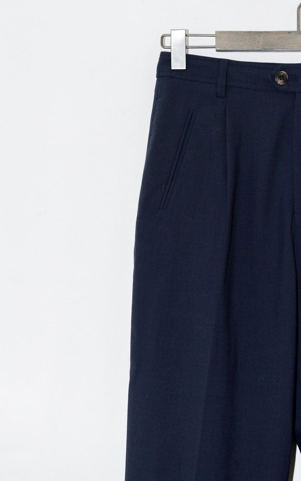 Geschlossene Arlo-Hose &ndash; marineblaue Anzughose W26 h&auml;ngt auf einem h&ouml;lzernen Kleiderb&uuml;gel vor einem schlichten hellen Hintergrund, sodass nur die obere H&auml;lfte der Hose zu sehen ist.