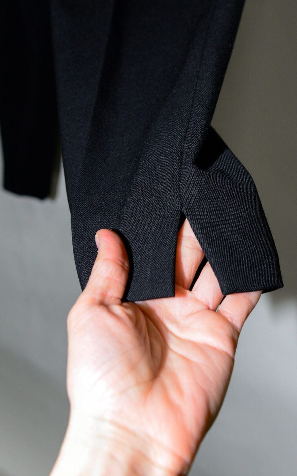 Eine Hand h&auml;lt den &Auml;rmel der Closed Arlo Hose &ndash; W26 und gibt den Blick auf ein Daumenloch im B&uuml;ndchen frei, wobei Licht die Textur des Stoffes hervorhebt.