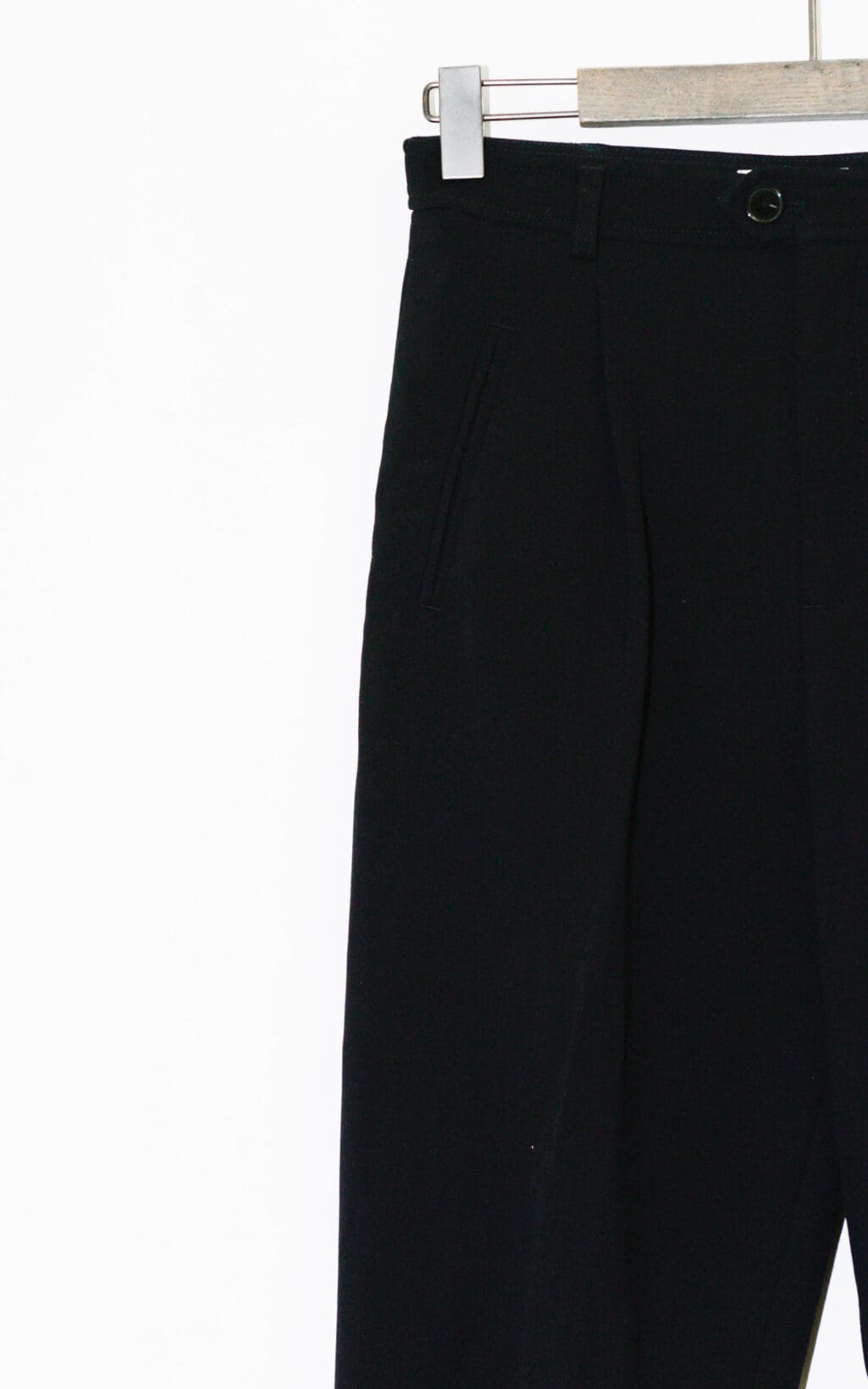 Die Closed Arlo Hose &ndash; W26, eine schwarze Anzughose, h&auml;ngt auf einem h&ouml;lzernen Kleiderb&uuml;gel vor einem schlichten wei&szlig;en Hintergrund, wobei nur der obere Teil sichtbar ist.