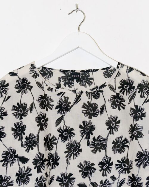 Das Sne Top – Gr. L mit schwarz-weißem Blumenmuster wird auf einem weißen Plastikbügel vor einem schlichten weißen Hintergrund präsentiert.