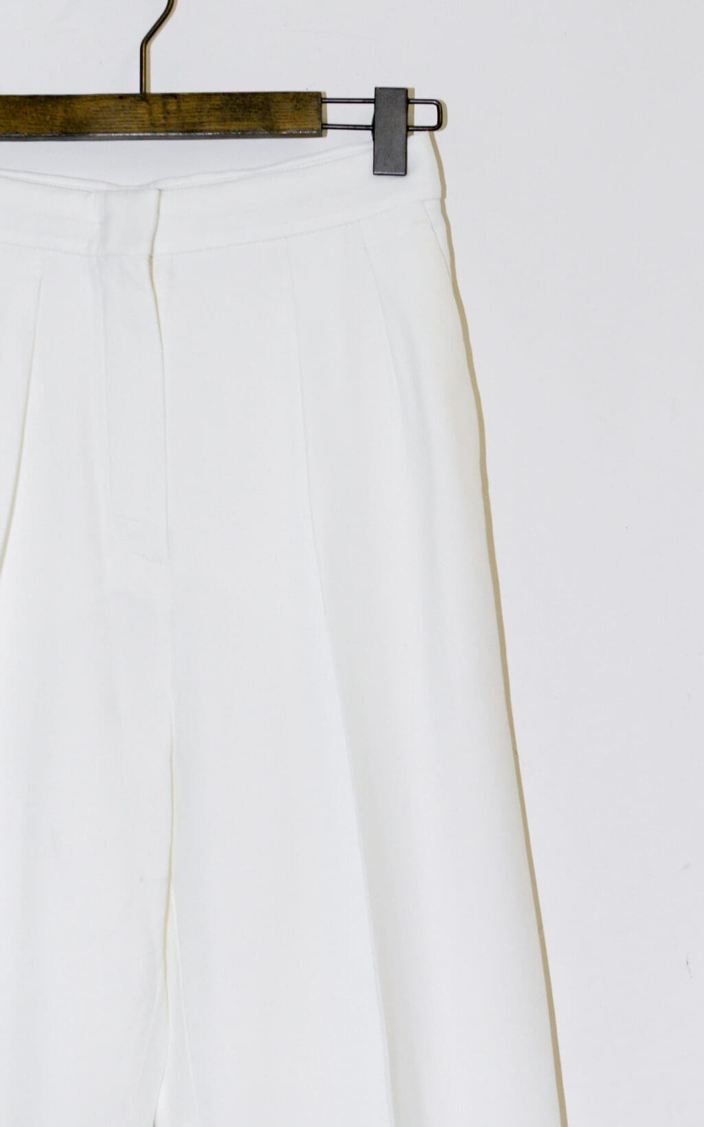 Eine hoch taillierte wei&szlig;e Hose von Sportmax Hose &ndash; Gr. 36 h&auml;ngt auf einem h&ouml;lzernen Kleiderb&uuml;gel vor einem schlichten wei&szlig;en Hintergrund.