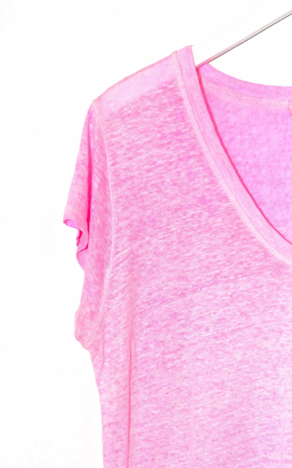 Leicht transparentes, pinkfarbenes Secondhand Leinen-T-Shirt von Alexander Laurent mit V-Ausschnitt und kurzen &Auml;rmeln, auf einem wei&szlig;en Kleiderb&uuml;gel vor hellem Hintergrund pr&auml;sentiert.