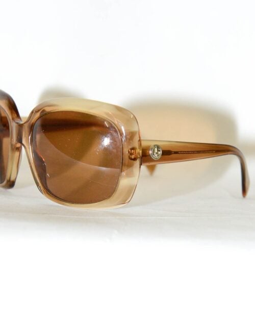 Nahaufnahme der Sonnenbrille von Giorgio Armani: braune, rechteckige Sonnenbrille mit durchscheinendem Rahmen, getönten Gläsern und einem kleinen runden Logodetail auf den Bügeln in der Nähe der Scharniere, auf einer weißen Oberfläche.