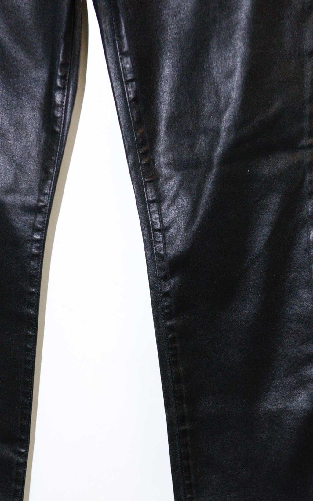 Schwarze beschichtete Jeans von J Brand in Lederoptik mit leichtem Schlag und klassischem 5-Pocket-Stil, auf einem Holzb&uuml;gel vor hellem Hintergrund pr&auml;sentiert.