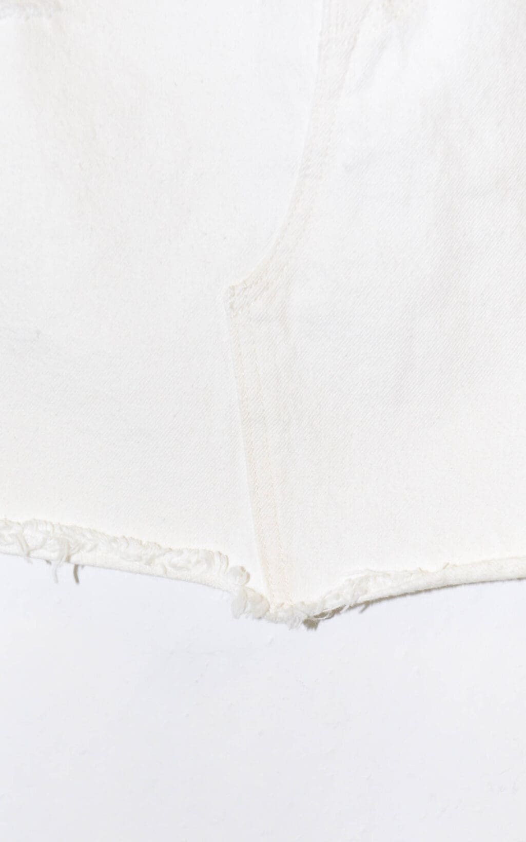 Nahaufnahme des ausgefransten Saums des Levi&lsquo;s Jeansrock &ndash; W26 aus wei&szlig;em Denim, der die Stoffstruktur und die N&auml;hte vor einem wei&szlig;en Hintergrund zeigt.
