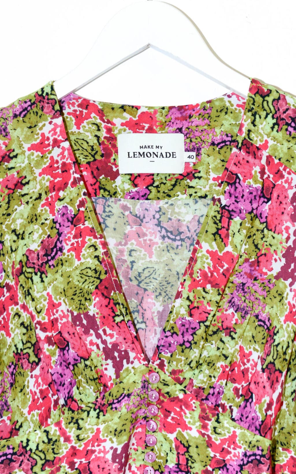 Nahaufnahme des Lemonade Fleurie Kleides &ndash; Gr. 40 mit farbenfrohem Blumenmuster in Rosa, Gr&uuml;n, Rot und Lila. Das Kleid hat einen V-Ausschnitt, kleine Kn&ouml;pfe vorne und ein &bdquo;Make My Lemonade&ldquo;-Etikett im Kragen.