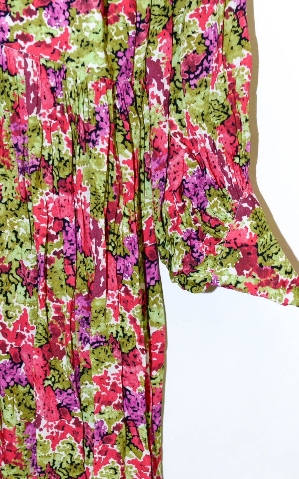 Eine Nahaufnahme des Lemonade Fleurie Kleides (Gr. 40), ein farbenfrohes, lang&auml;rmliges Plisseekleid mit floralem Muster in Gr&uuml;n, Rosa, Lila und Rot auf Wei&szlig;. Ein &Auml;rmel ist seitlich leicht verl&auml;ngert.