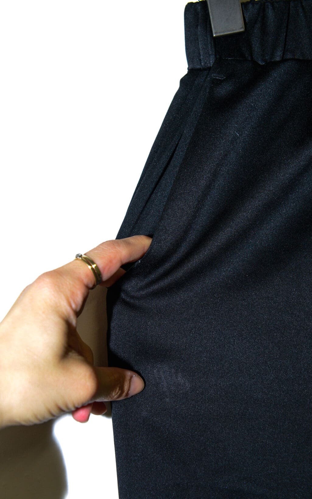 Eine Hand mit Ringen zupft an der Tasche einer schwarzen Hose der Maxmara Leisure Hose &ndash; Gr. S und demonstriert so die Struktur und Dehnbarkeit des Stoffes vor einem schlichten wei&szlig;en Hintergrund.