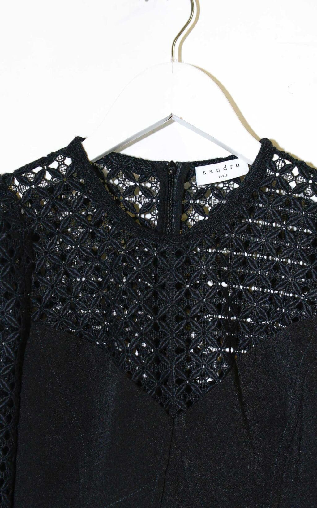 Schwarzes Secondhand Kleid von Sandro mit Spitzenoberteil, 3/4-&Auml;rmeln und tailliertem Schnitt, auf einem wei&szlig;en Kleiderb&uuml;gel vor hellem Hintergrund pr&auml;sentiert.