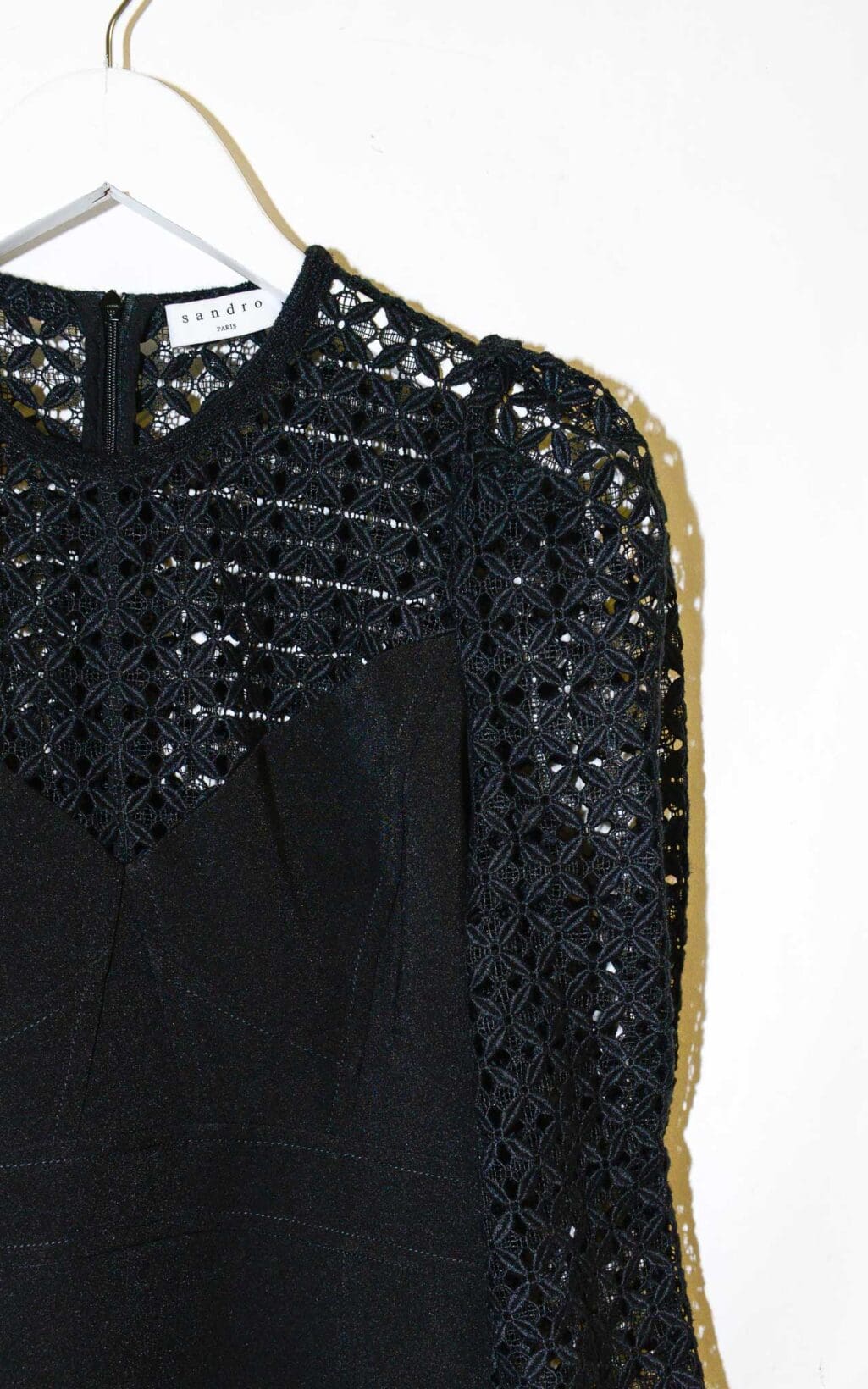 Schwarzes Secondhand Kleid von Sandro mit Spitzenoberteil, 3/4-&Auml;rmeln und tailliertem Schnitt, auf einem wei&szlig;en Kleiderb&uuml;gel vor hellem Hintergrund pr&auml;sentiert.
