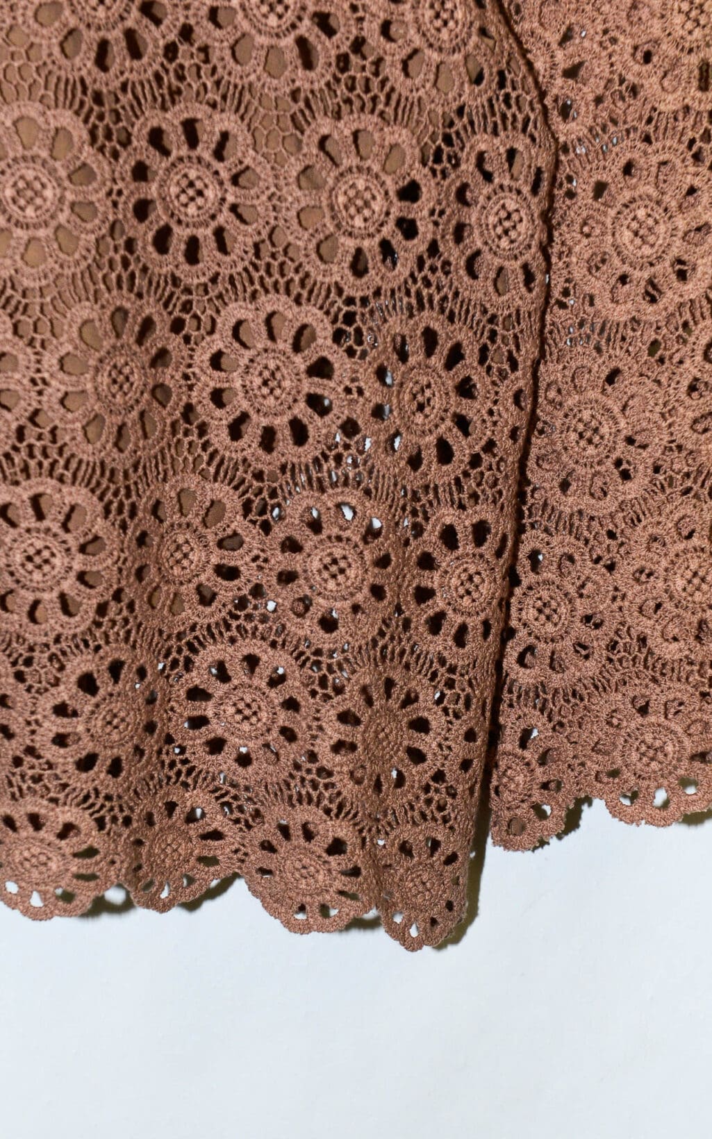 Nahaufnahme des Deen & Keenu Lace Crop Top (Gr. L): brauner H&auml;kelstoff mit sich wiederholenden Blumenmotiven, komplizierten Spitzendetails und einem gewellten Rand vor hellem Hintergrund.