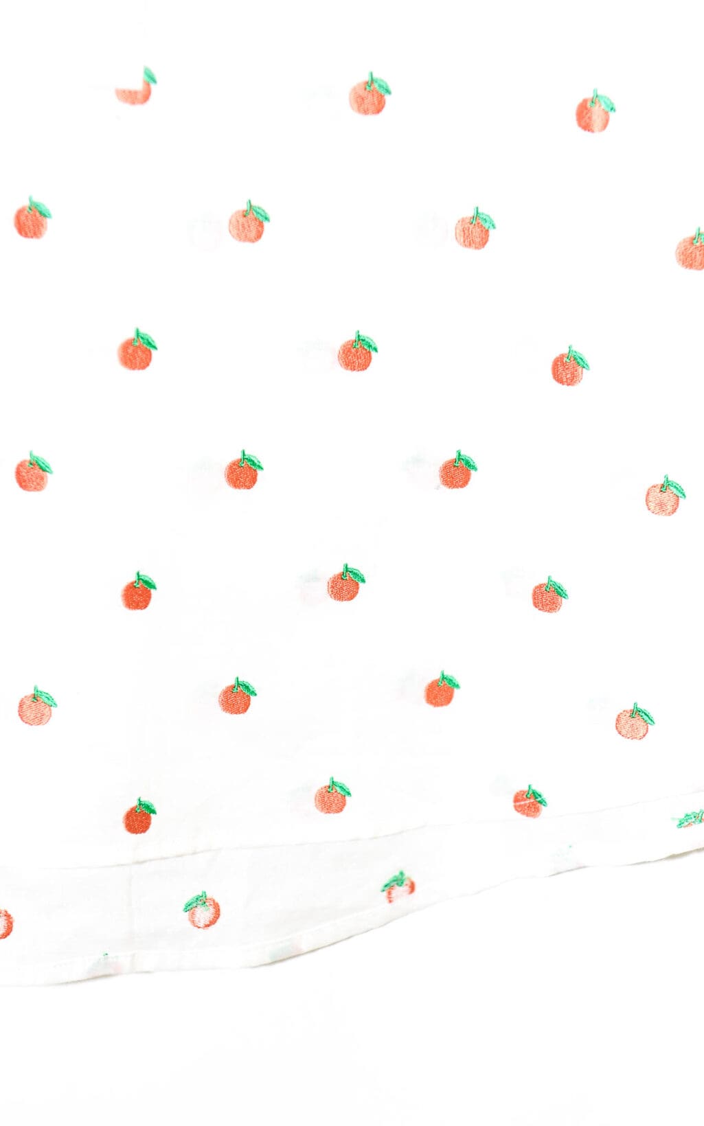Deen & Keenu Bluse – in verschiedenen Größen: Weiße Bluse mit gleichmäßig verteiltem Muster aus kleinen, orangefarbenen Früchten mit grünen Blättern, die an Orangen oder Mandarinen erinnern.
