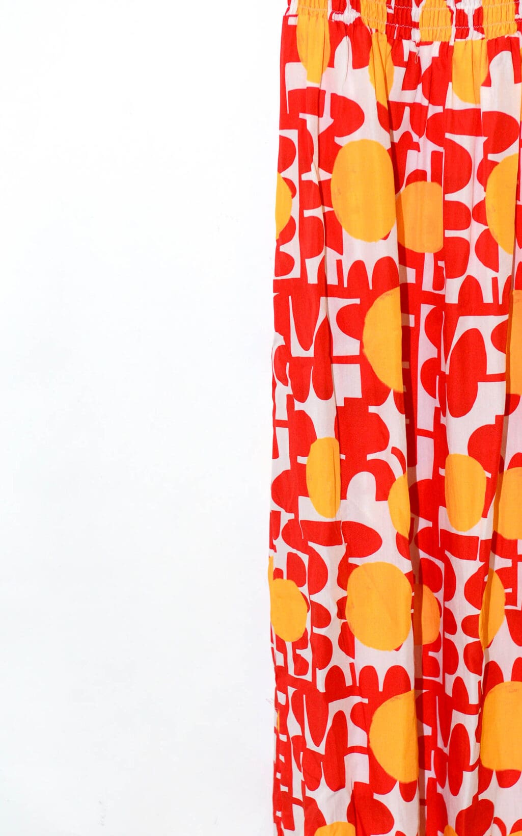 Eine Nahaufnahme des Maxikleids (Gr. 40) von Elise Chalmin Paris zeigt sein leuchtend rotes und gelbes abstraktes Blumenmuster auf wei&szlig;em Stoff, komplett mit elastischem Bund.