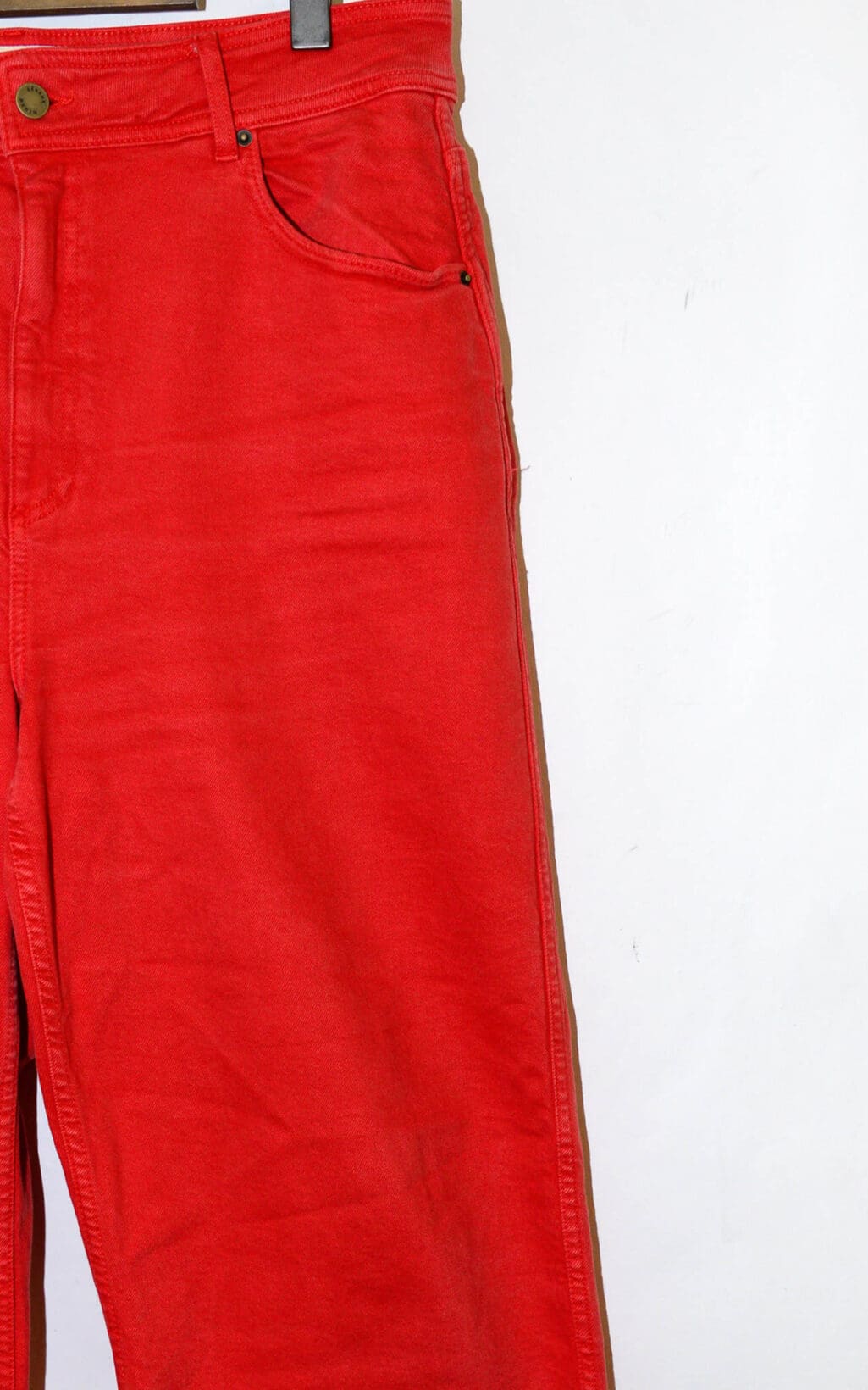 Auf einem B&uuml;gel vor schlichtem wei&szlig;em Untergrund h&auml;ngt eine S&eacute;zane Wideleg Jeans (Gr. 44) in leuchtendem Rot, wobei nur der obere linke Bereich &ndash; Bund, Vordertasche und Knopf &ndash; vollst&auml;ndig sichtbar ist.