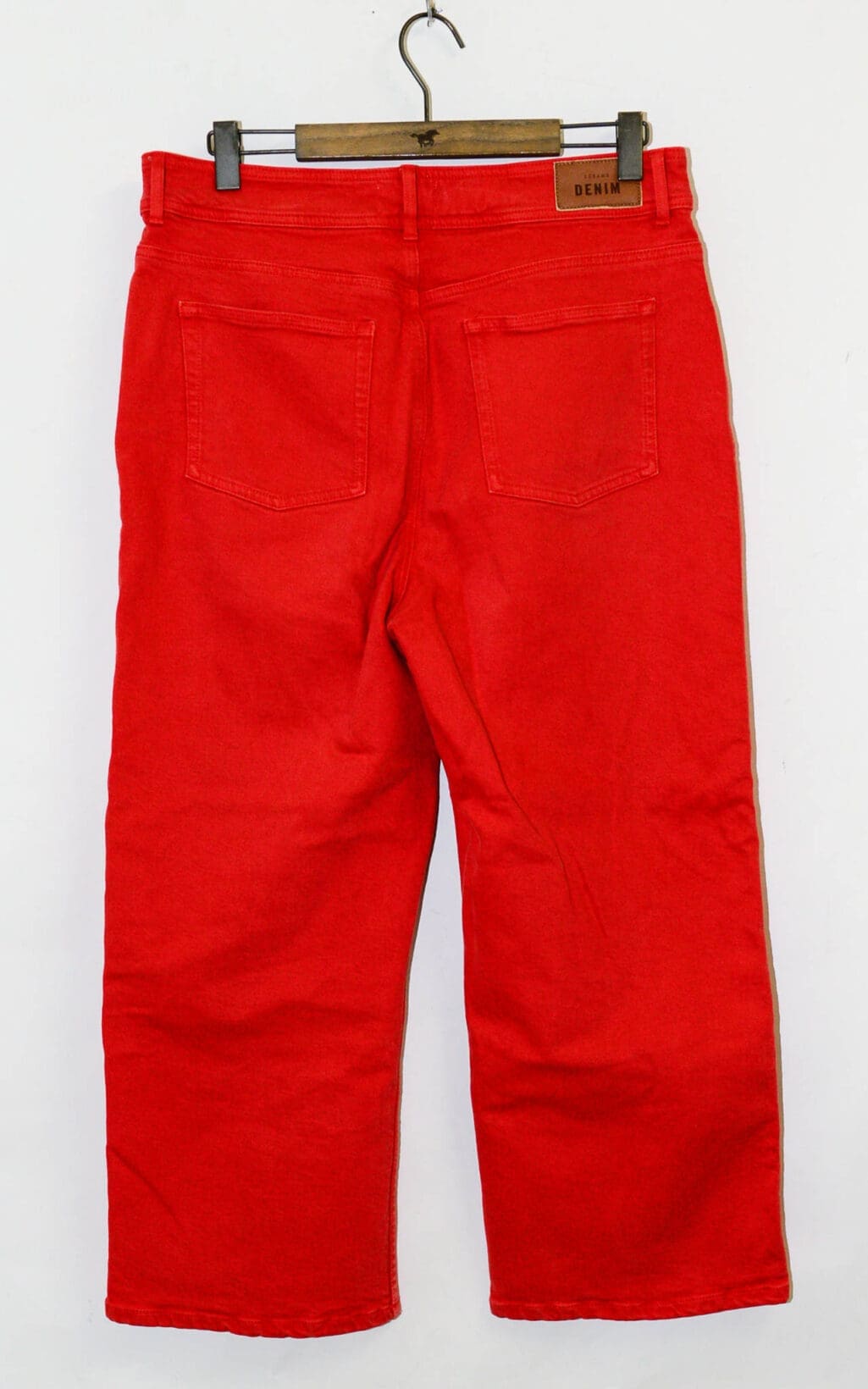 S&eacute;zane Wideleg Jeans &ndash; Gr. 44 in leuchtend rotem Denim, von hinten auf einem Holzb&uuml;gel abgebildet, mit zwei Ges&auml;&szlig;taschen und einem braunen Leder-Patch-Label am Hosenbund, abgebildet auf wei&szlig;em Hintergrund.