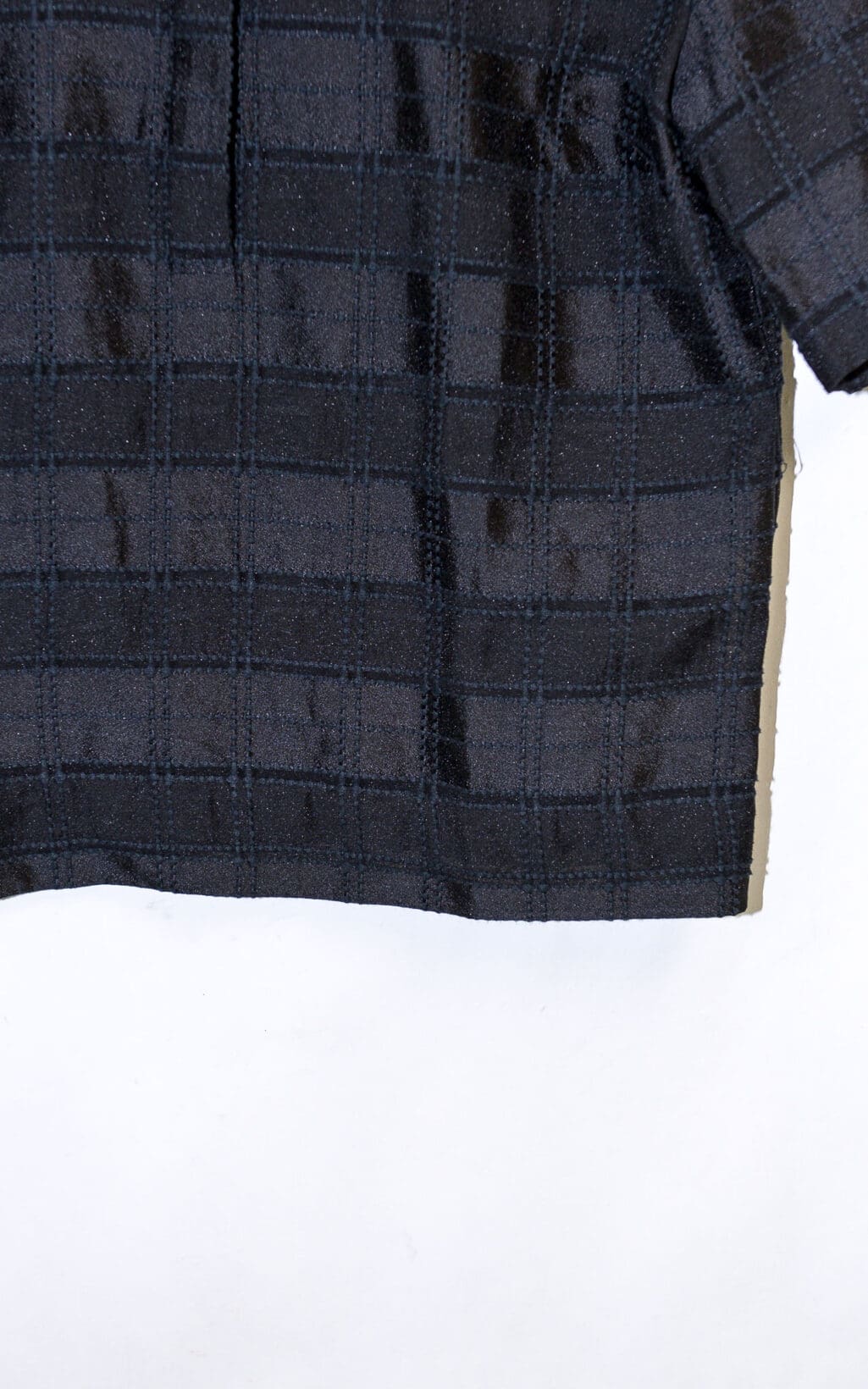 Eine Nahaufnahme der Globus &bdquo;Doha&ldquo;-Bluse in Gr&ouml;&szlig;e 40 mit schwarzen kurzen &Auml;rmeln und strukturiertem Gittermuster, teilweise vor wei&szlig;em Hintergrund.