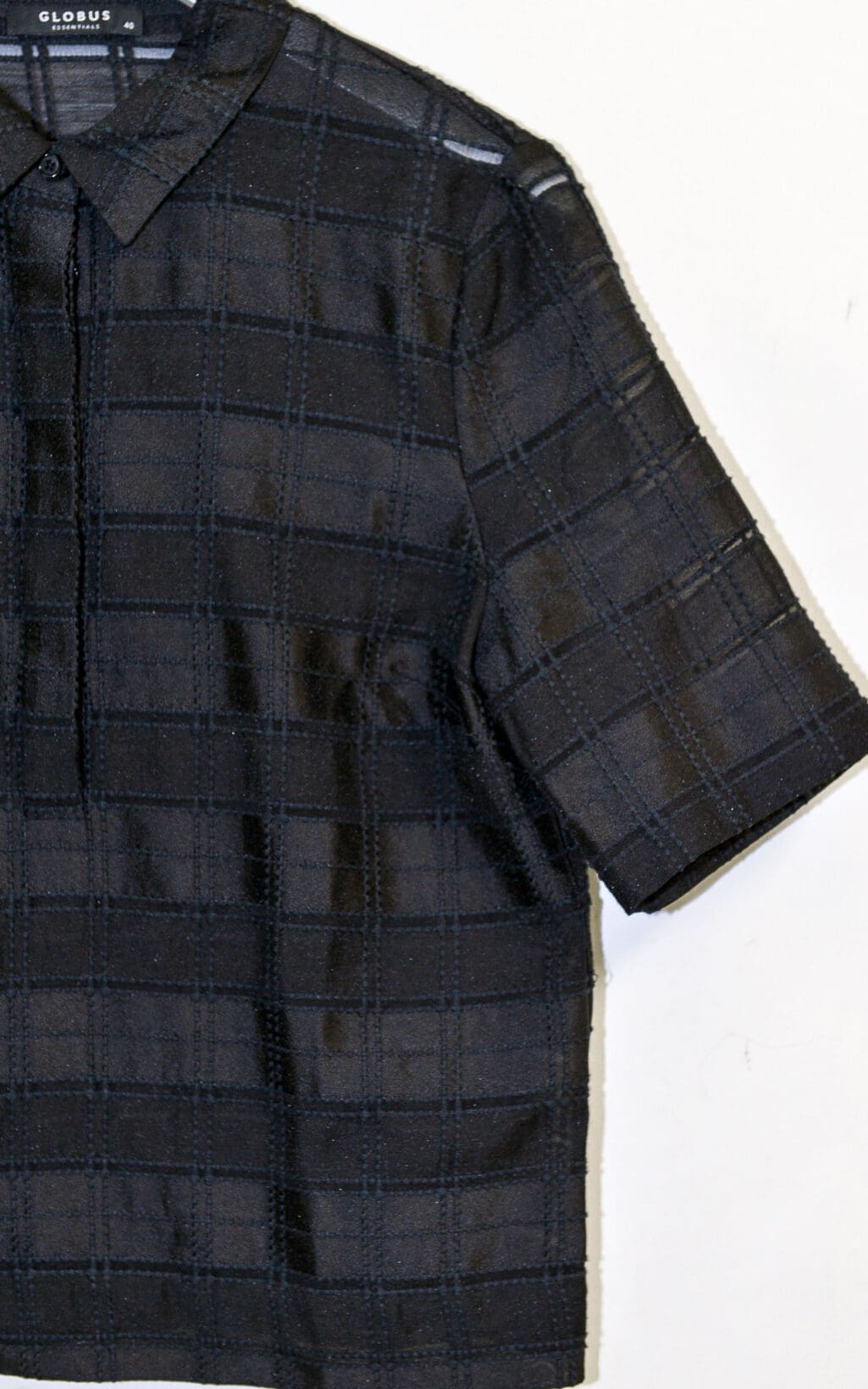 Die Globus &bdquo;Doha&ldquo; Bluse &ndash; Gr. 40 ist eine kurz&auml;rmelige, schwarz karierte Bluse mit Kragen und Knopfleiste auf schlichtem wei&szlig;em Grund. Das dezente Gittermuster verleiht ihr zus&auml;tzlichen Stil.