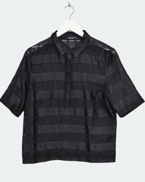 Globus &bdquo;Doha&ldquo; Bluse in Gr&ouml;&szlig;e 40: Schwarze Kurzarmbluse mit kariertem, transparentem Muster, Kragen und halber Knopfleiste, pr&auml;sentiert auf wei&szlig;em B&uuml;gel vor hellem Hintergrund.