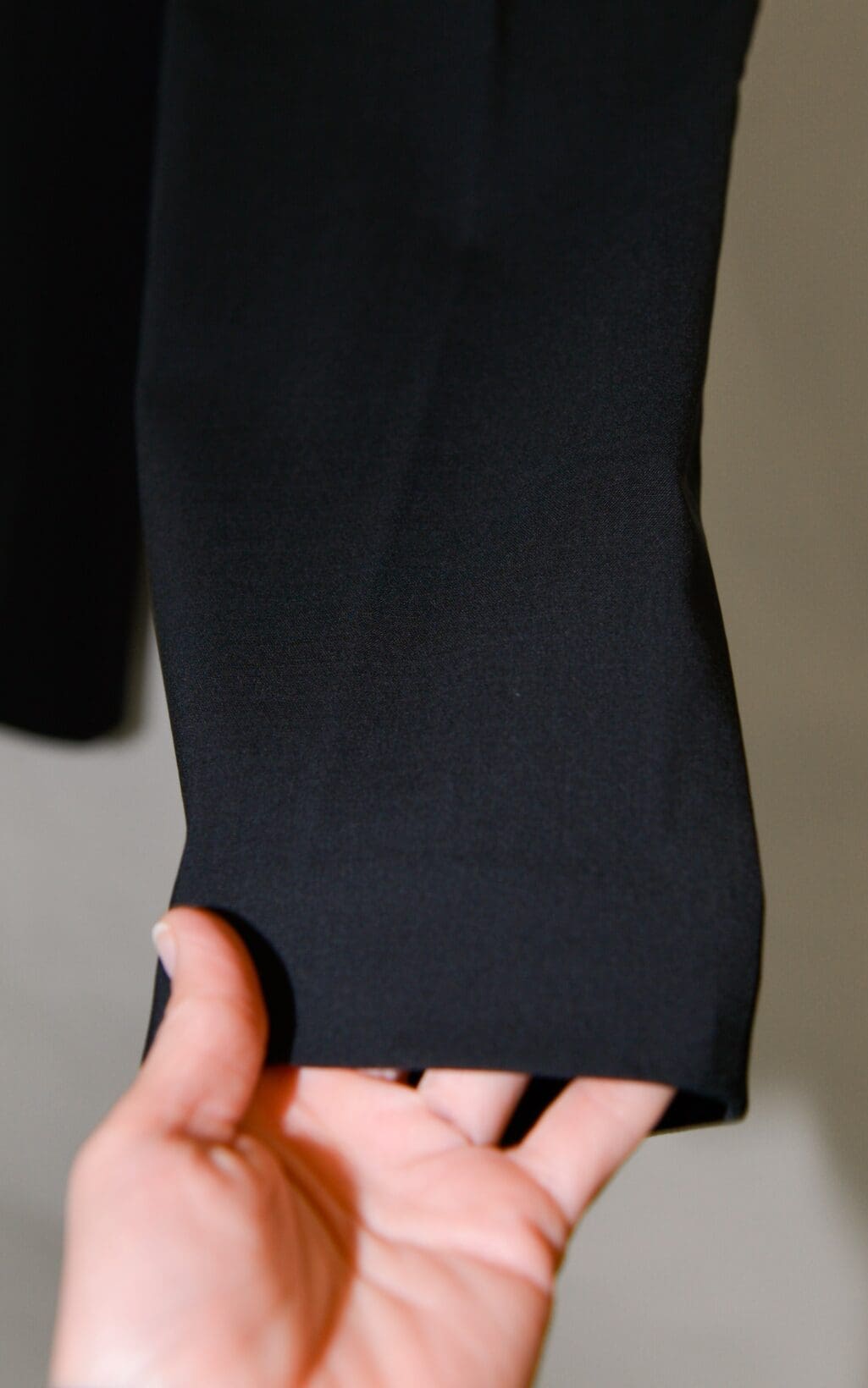 Eine Nahaufnahme der Hand einer Person, die sanft den Saum einer schwarzen Hose der Marke Theory Hose (Gr. 36) vor einem neutralen Hintergrund h&auml;lt.