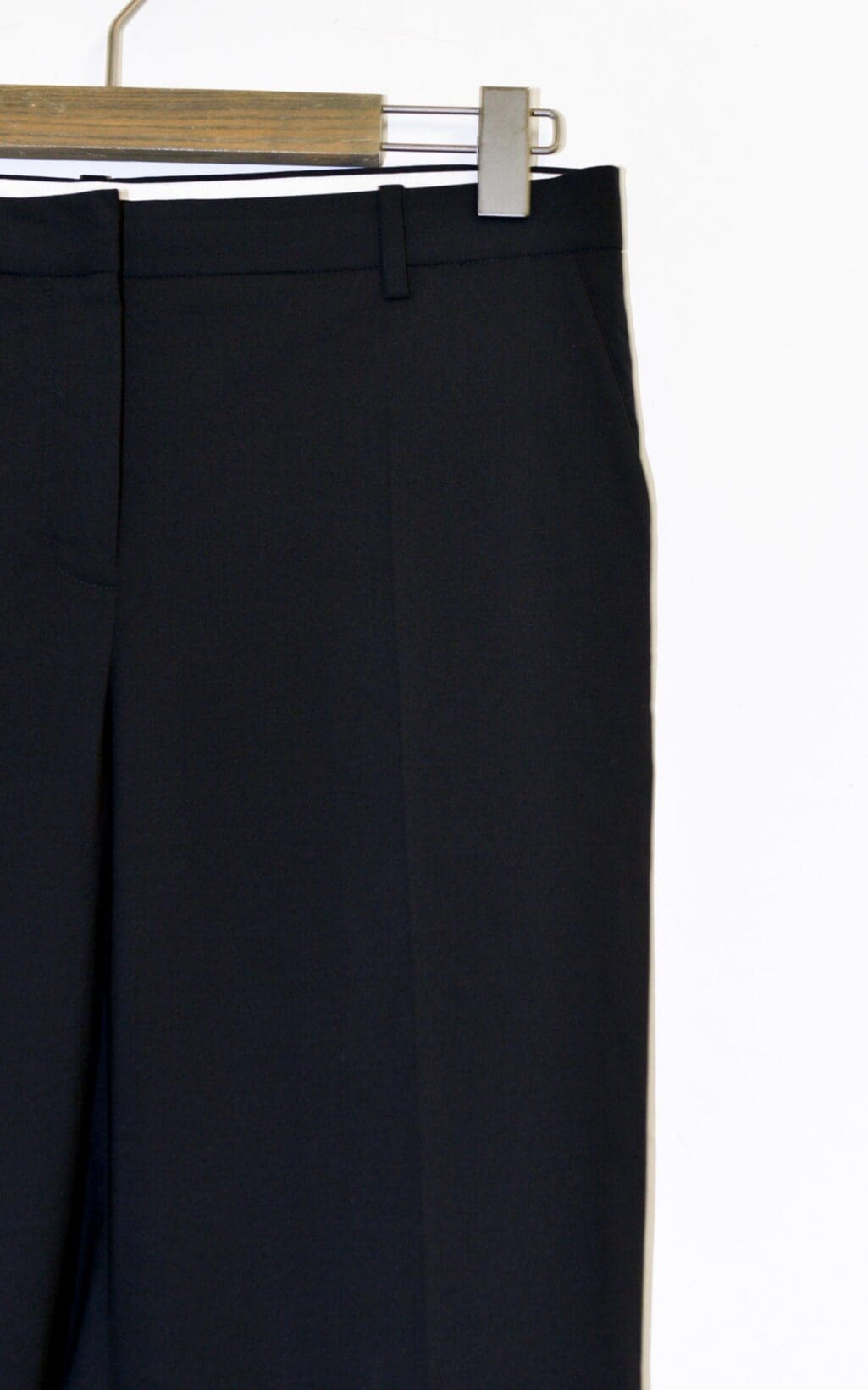 Theory Hose - Gr. 36 in Schwarz, pr&auml;sentiert auf einem Holzb&uuml;gel vor schlichtem wei&szlig;en Hintergrund. Nur der obere Teil der Hose und der B&uuml;gel sind sichtbar.