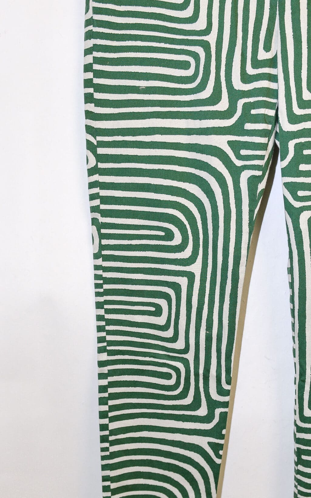 Nahaufnahme der EMME Marella Hose (Gr. 40) mit einem gr&uuml;n-wei&szlig;en abstrakten Labyrinthmuster mit geschwungenen, miteinander verbundenen Linien. Nur ein Teil des linken Hosenbeins und ein kleiner Teil des rechten sind sichtbar.