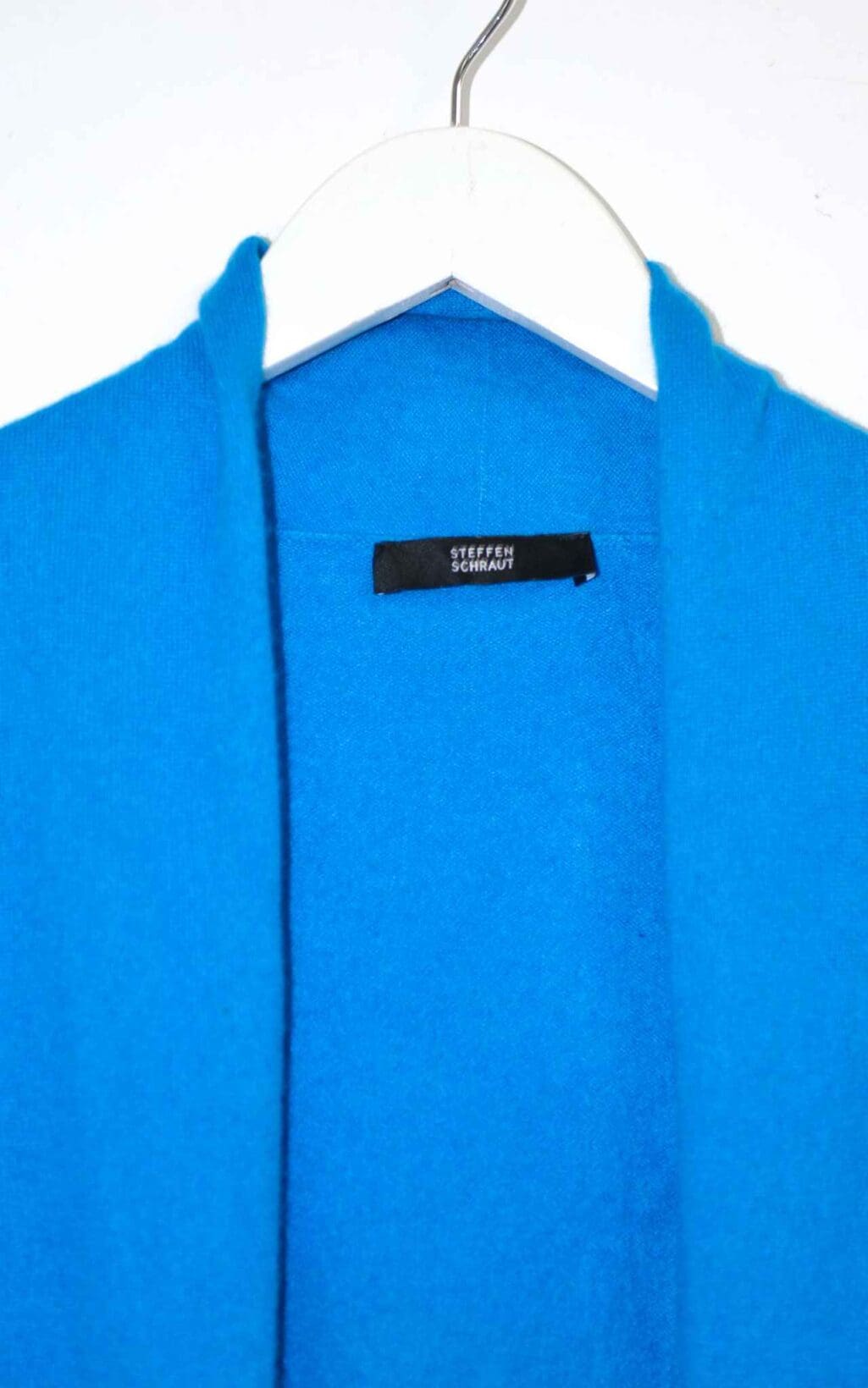 Eine Nahaufnahme einer hellblauen Steffen Schraut Strickjacke aus 100% Kaschmir (Gr. 40) auf einem wei&szlig;en Kleiderb&uuml;gel, die den Kragen und das schwarze Etikett mit wei&szlig;em Text im Halsausschnitt zeigt.