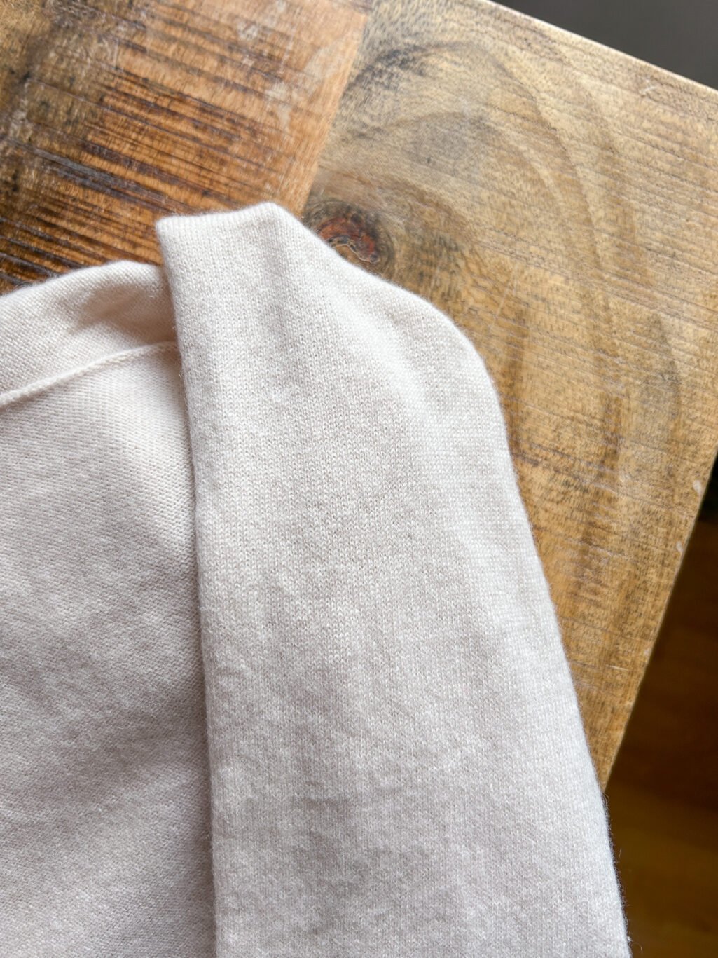 Rena Marx Kaschmir Cardigan in Ecru. Secondhand. Gefaltet auf Holztisch.