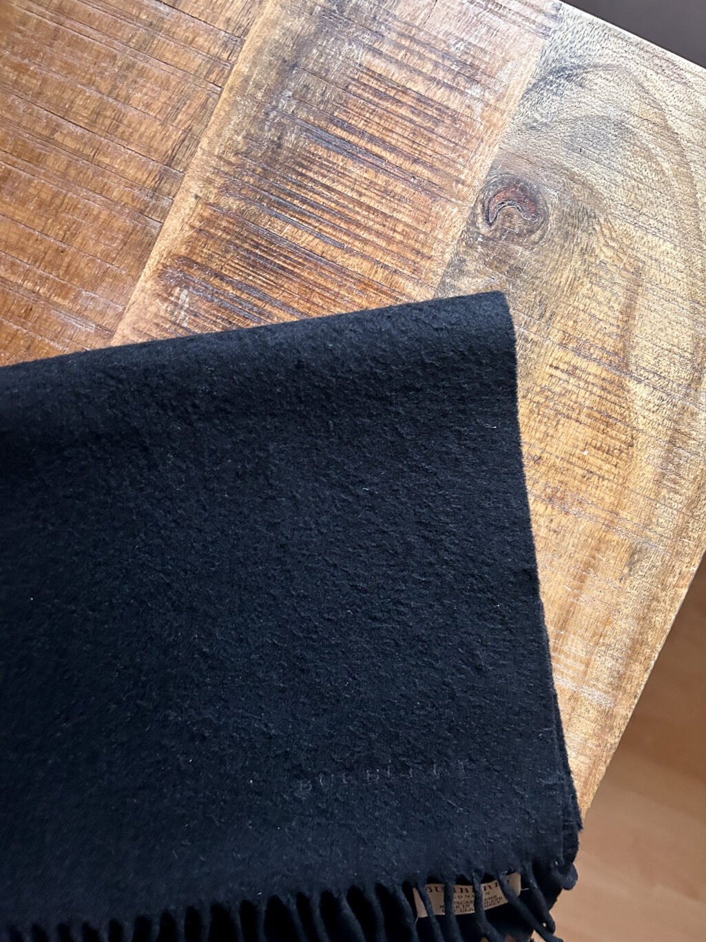 Schwarzer Secondhand Kaschmir Schal von Burberry gefaltet auf Holztisch.