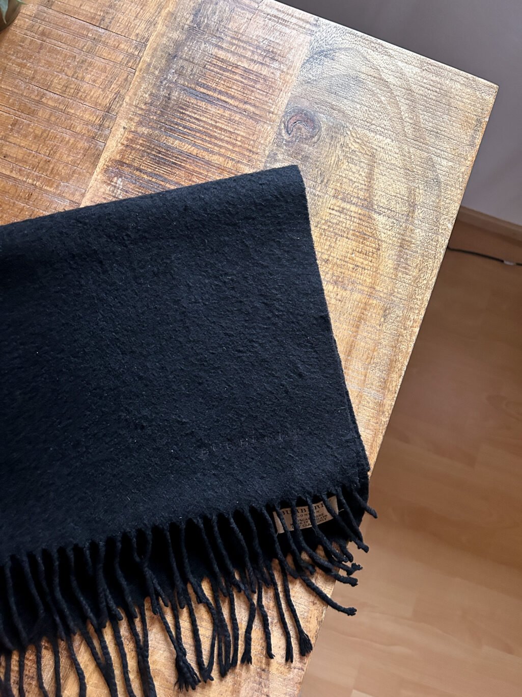 Schwarzer Secondhand Kaschmir Schal von Burberry gefaltet auf Holztisch.