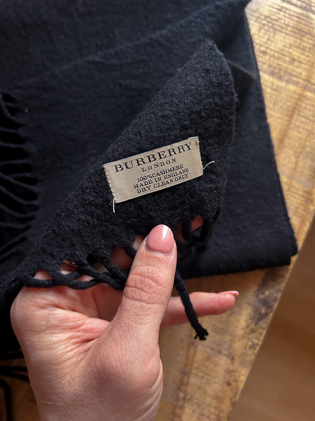 Schwarzer Secondhand Kaschmir Schal von Burberry gefaltet auf Holztisch.