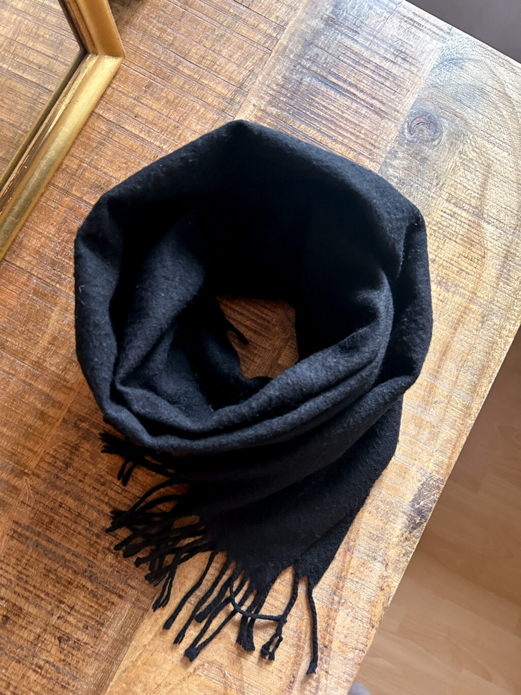 Schwarzer Secondhand Kaschmir Schal von Burberry gefaltet auf Holztisch.