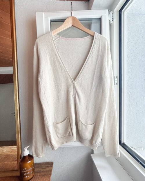 Secondhand Kaschmir Cardigan von Herzen's Angelegenheit in Ecru, h&auml;ngend am Holzb&uuml;gel.