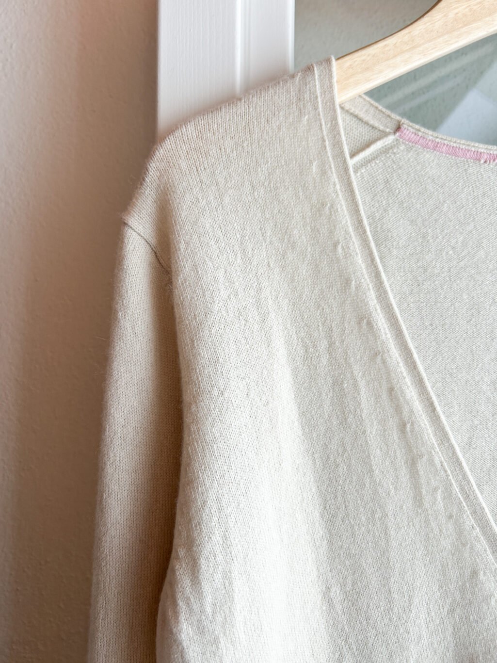 Secondhand Kaschmir Cardigan von Herzen's Angelegenheit in Ecru, gefaltet auf Holztisch.