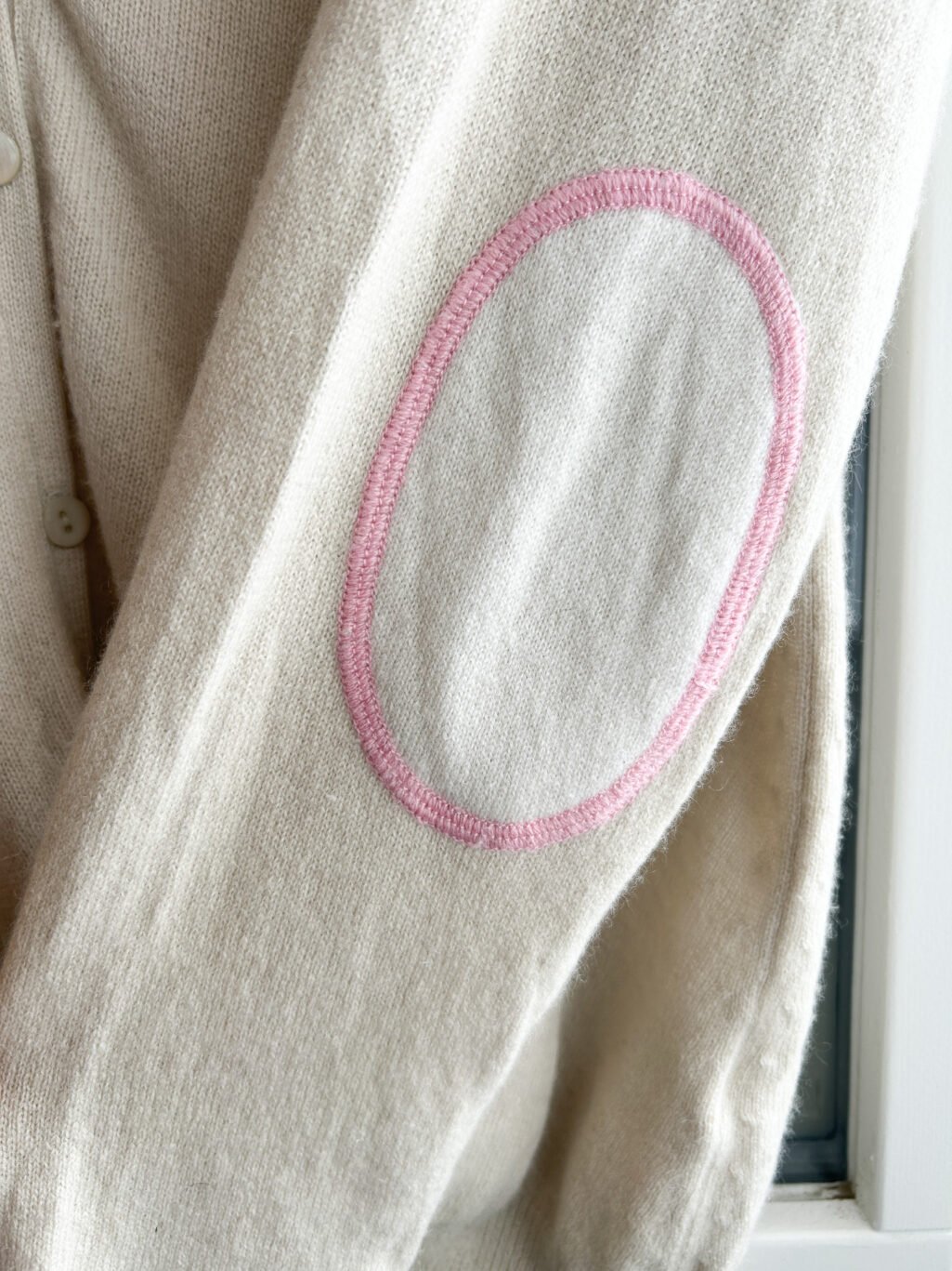 Secondhand Kaschmir Cardigan von Herzen's Angelegenheit in Ecru, gefaltet auf Holztisch.