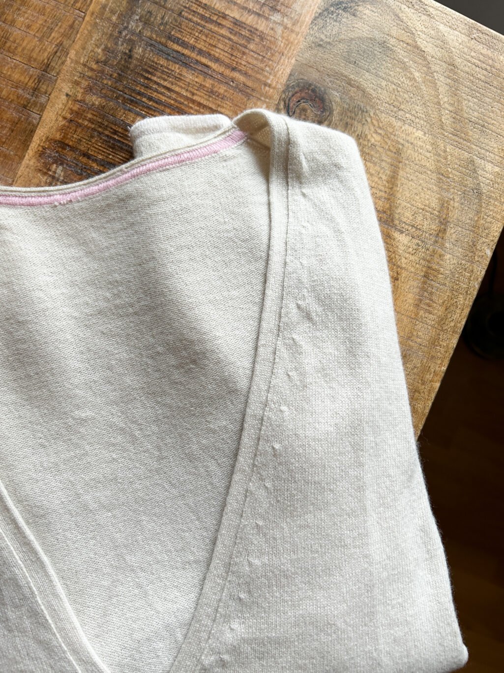 Secondhand Kaschmir Cardigan von Herzen's Angelegenheit in Ecru, gefaltet auf Holztisch.