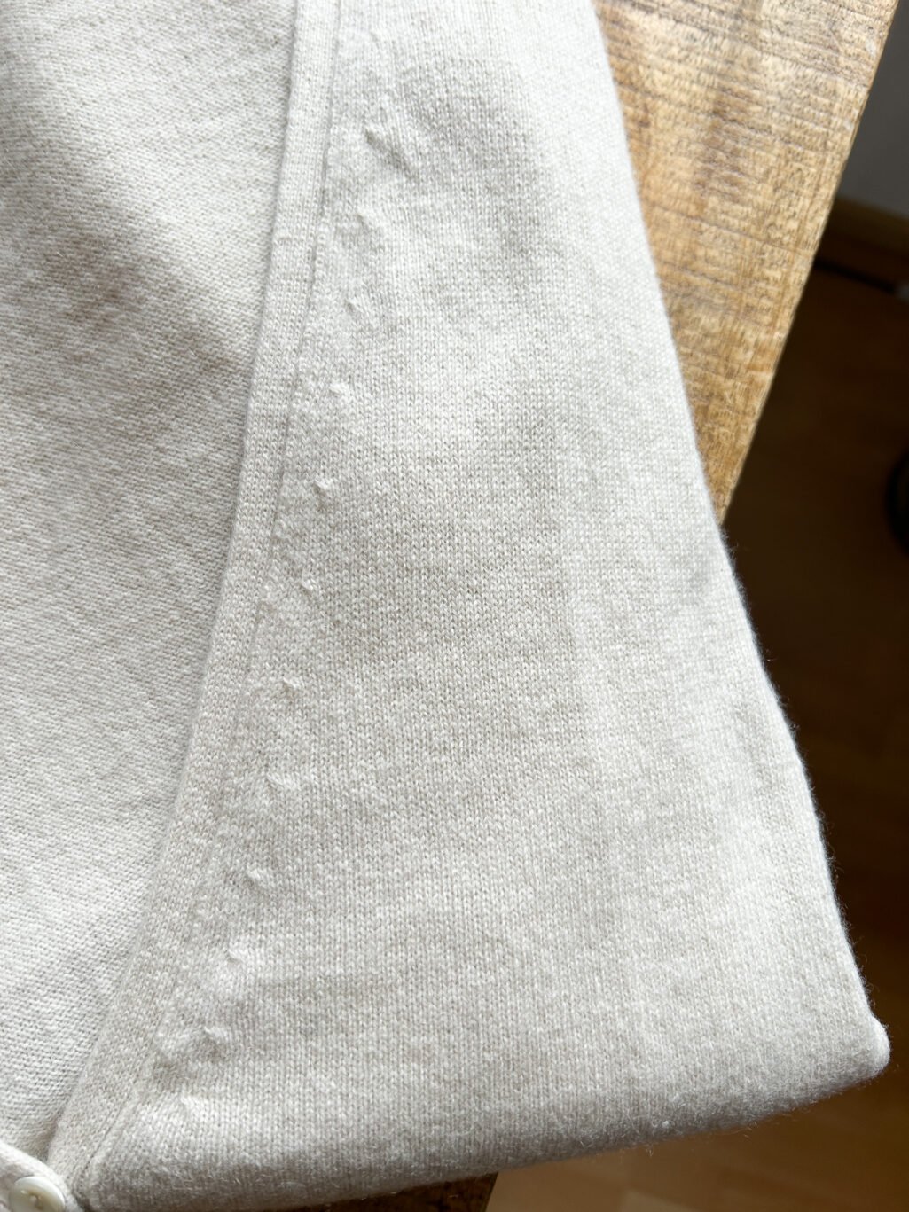 Secondhand Kaschmir Cardigan von Herzen's Angelegenheit in Ecru, gefaltet auf Holztisch.