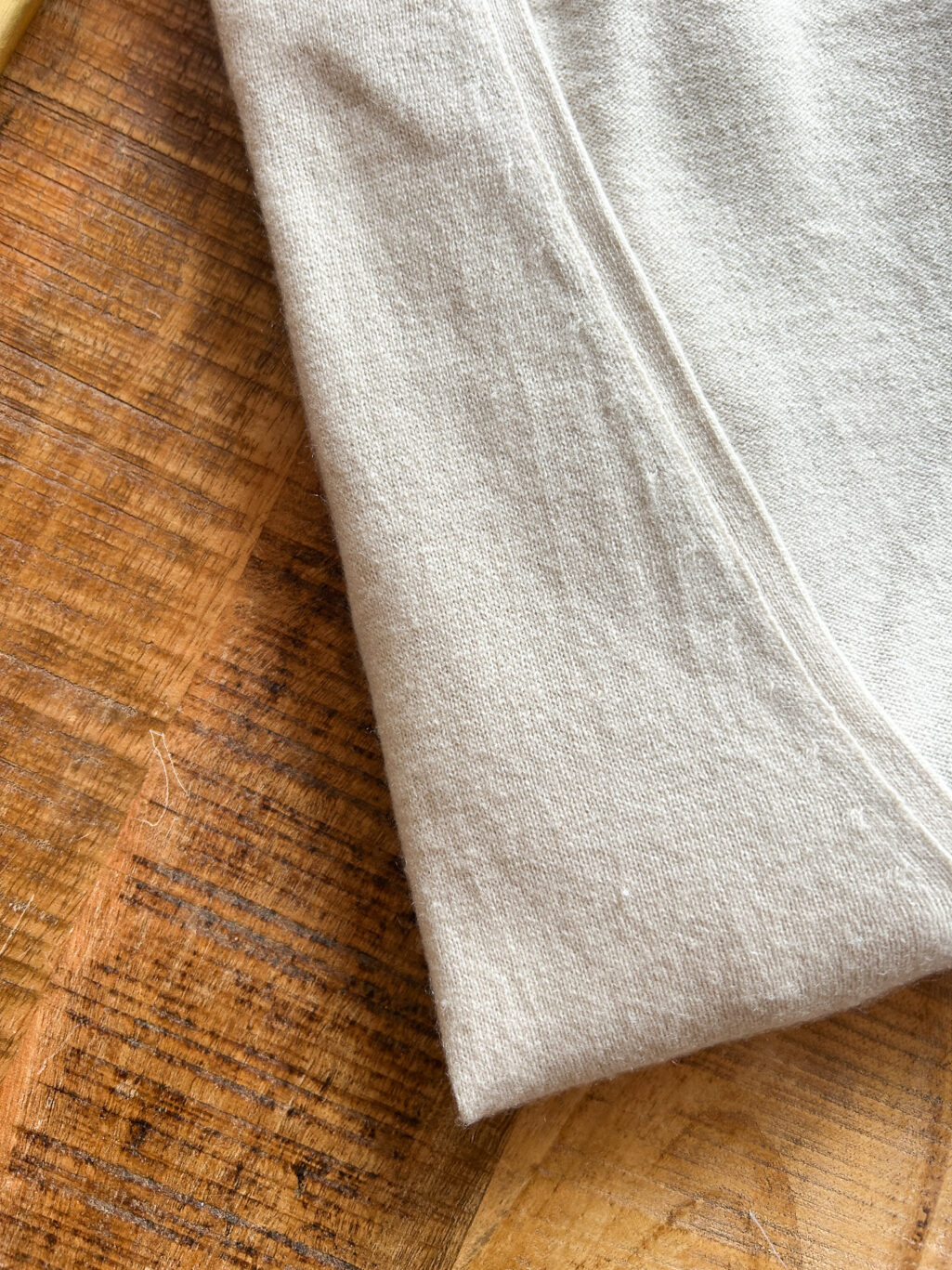 Secondhand Kaschmir Cardigan von Herzen's Angelegenheit in Ecru, gefaltet auf Holztisch.