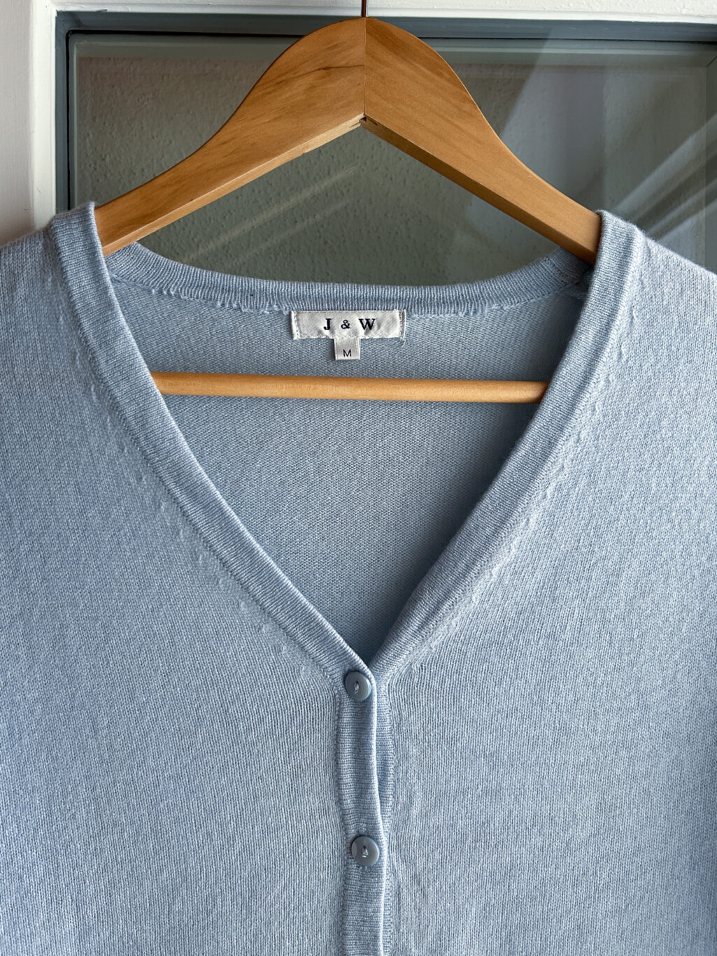 J&W Cashmere Cardigan in Hellblau mit Kn&ouml;pfen und V-Ausschnitt. Preloved, h&auml;ngend an Kleiderb&uuml;gel.
