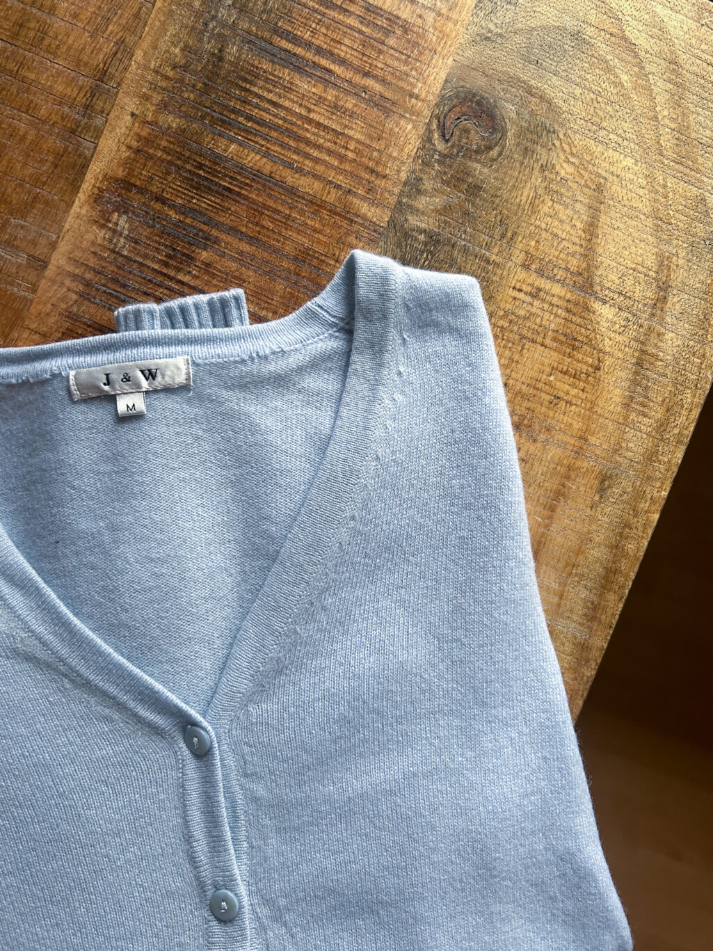 J&W Cashmere Cardigan in Hellblau mit Kn&ouml;pfen und V-Ausschnitt. Preloved, gefaltet auf Holztisch.