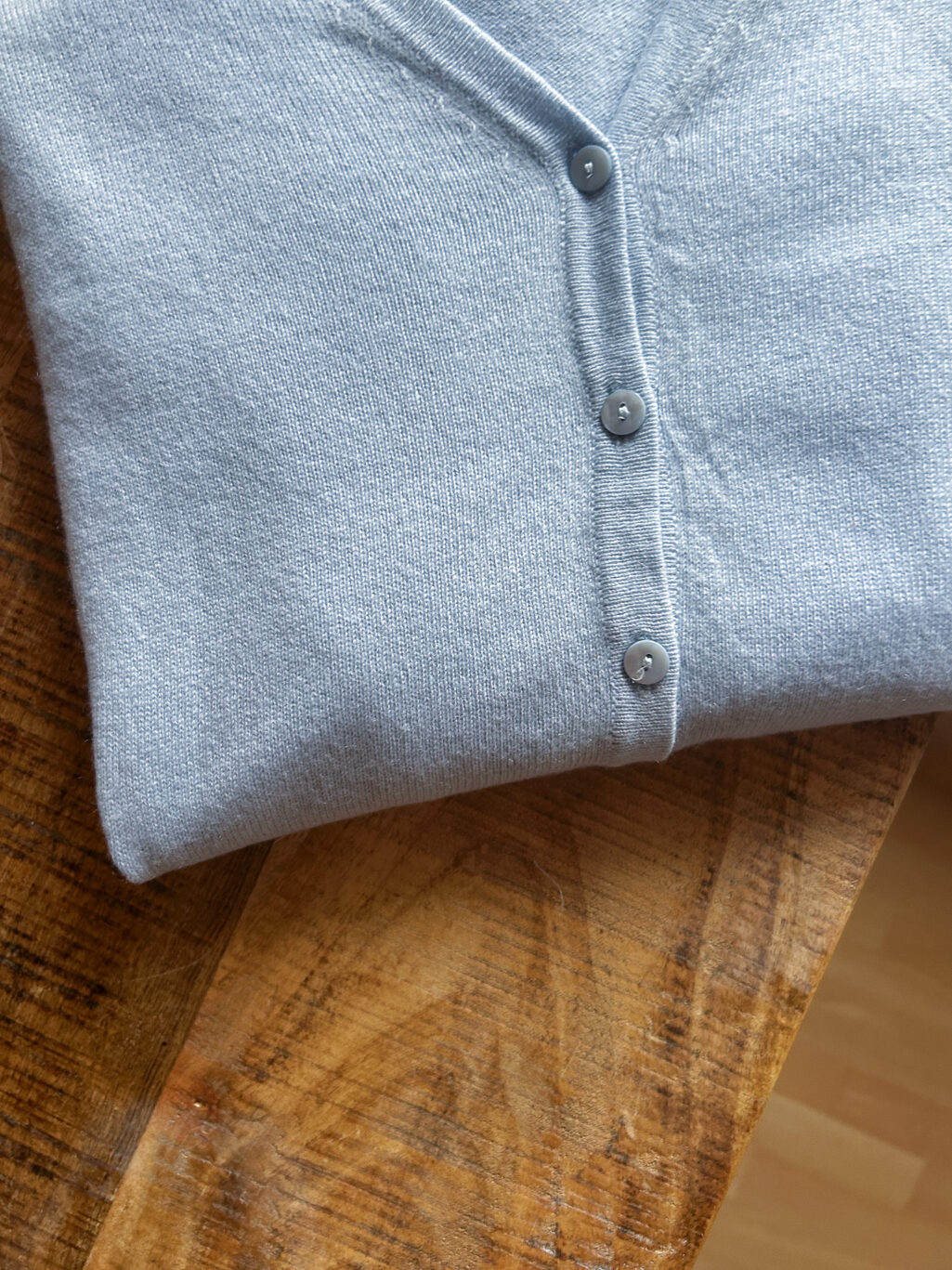 J&W Cashmere Cardigan in Hellblau mit Kn&ouml;pfen und V-Ausschnitt. Preloved, gefaltet auf Holztisch.