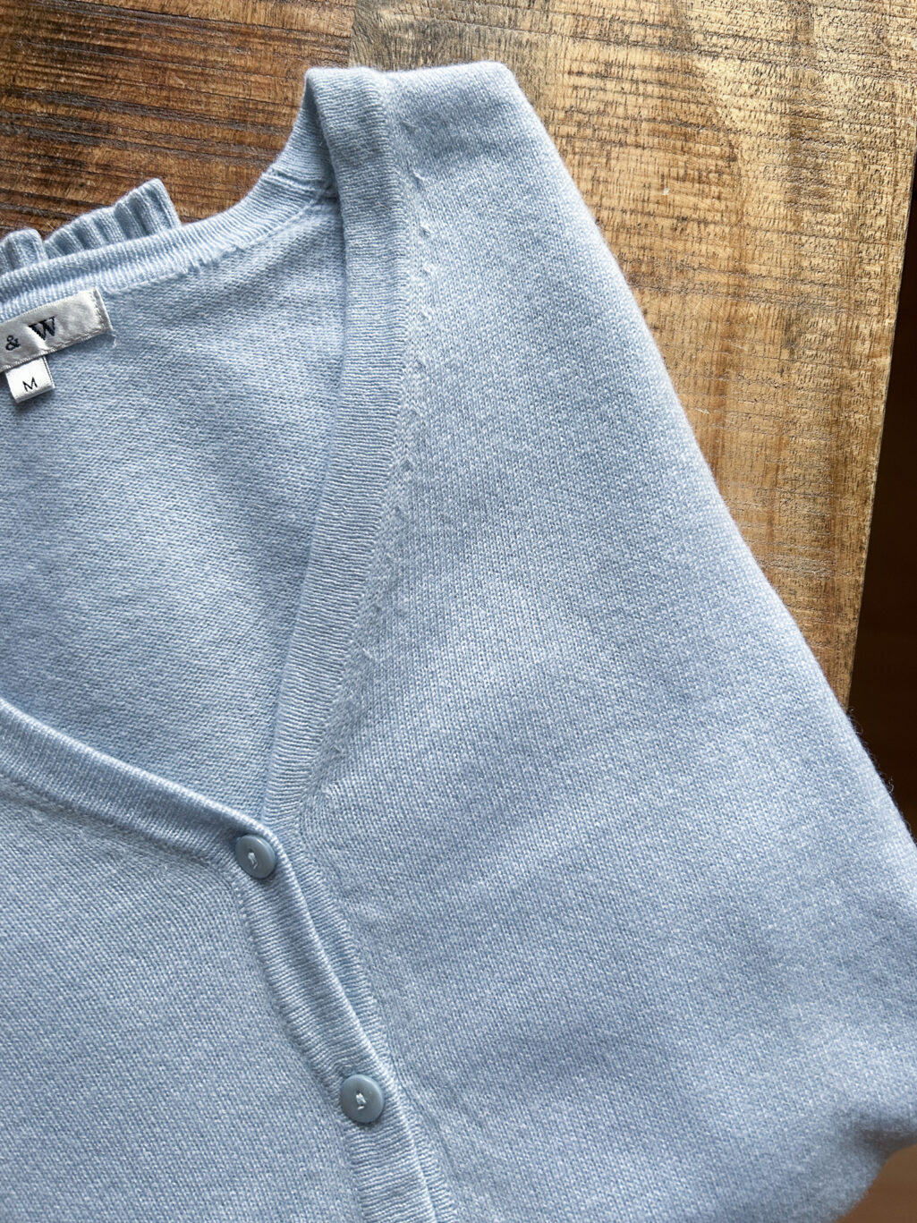 J&W Cashmere Cardigan in Hellblau mit Kn&ouml;pfen und V-Ausschnitt. Preloved, gefaltet auf Holztisch.